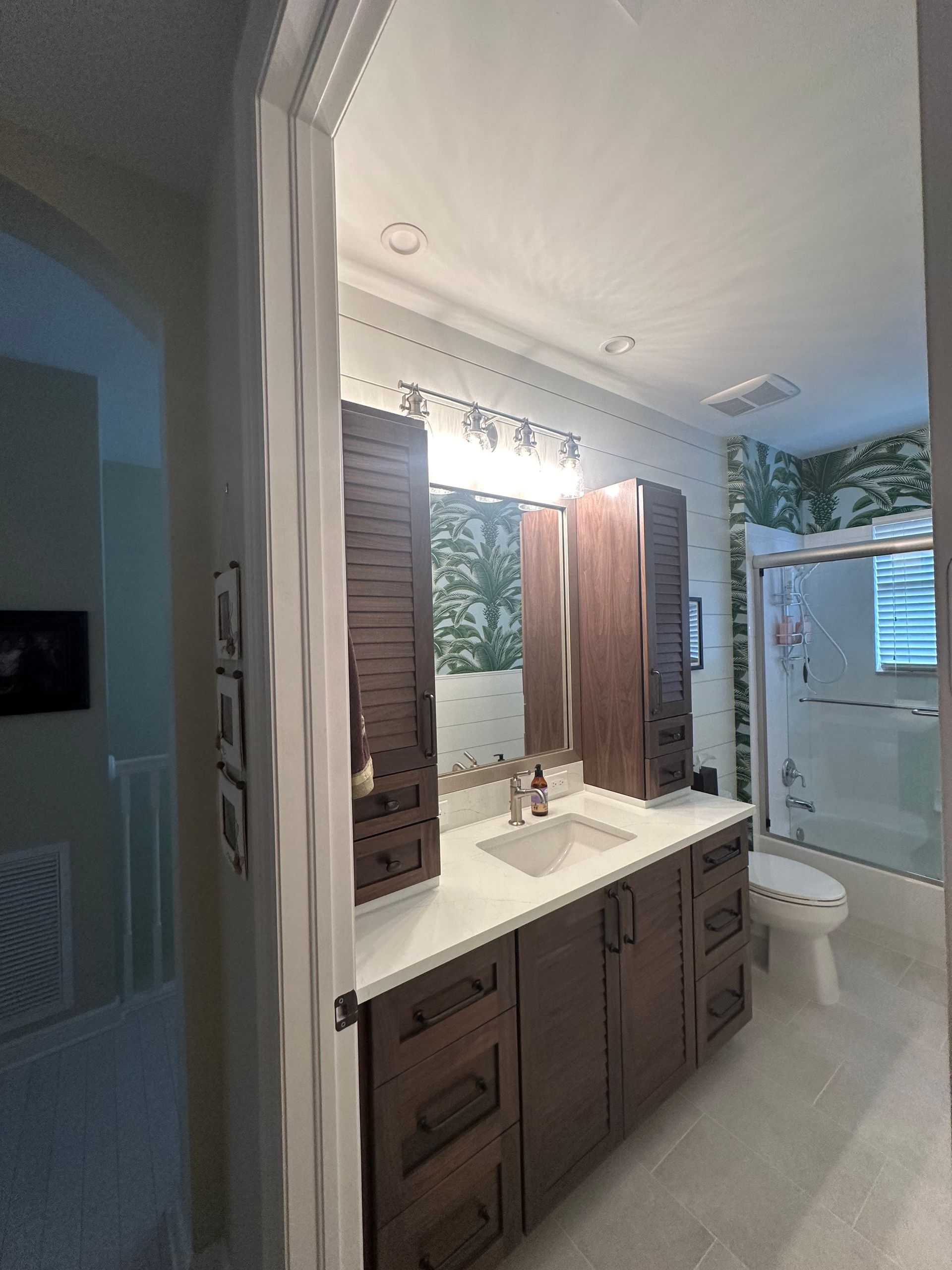 Bathroom with dark wood vanity, white countertop, and patterned wallpaper.