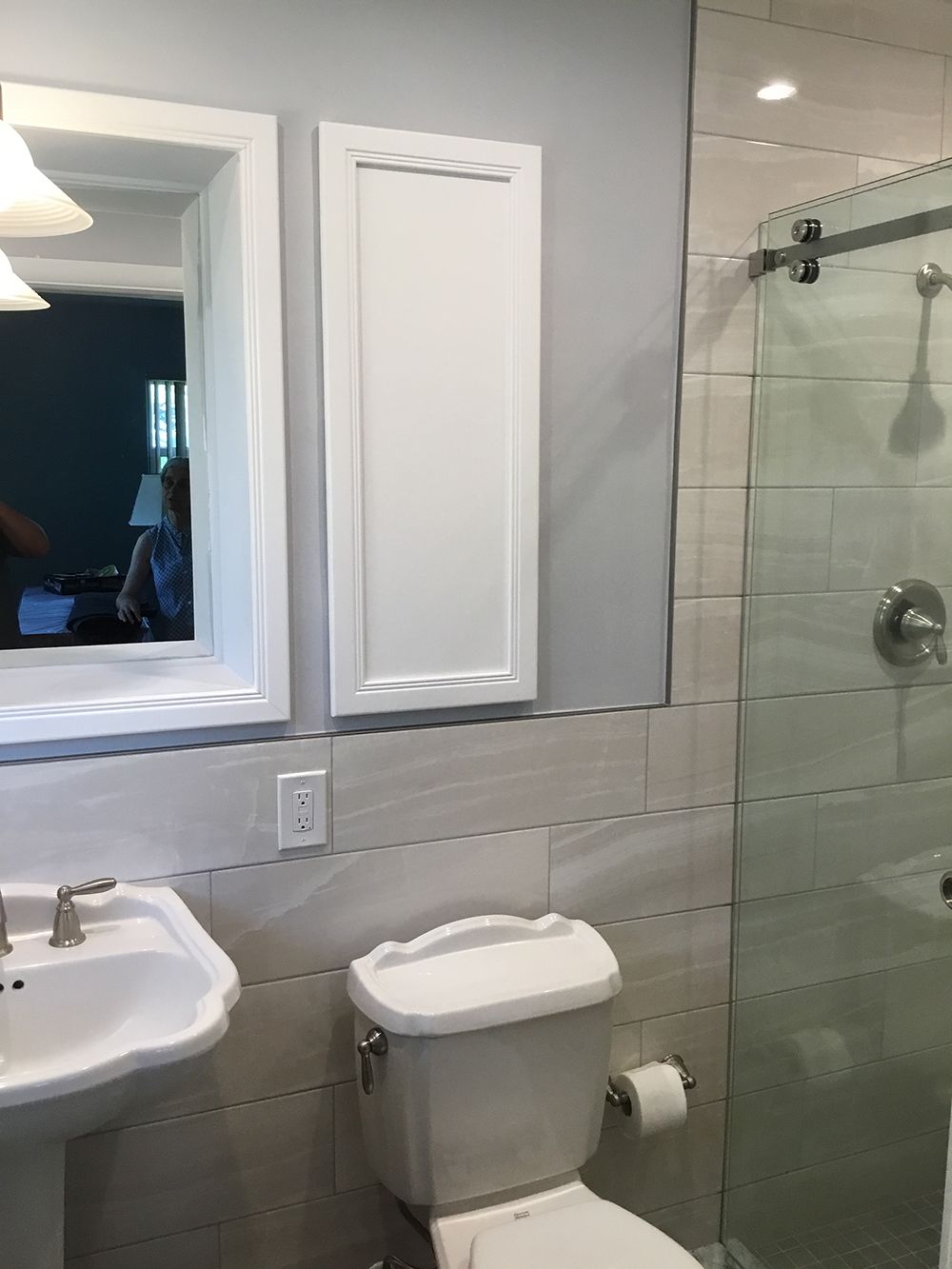Bathroom with sink, toilet, shower, mirror, and cabinet. Gray and white color scheme.
