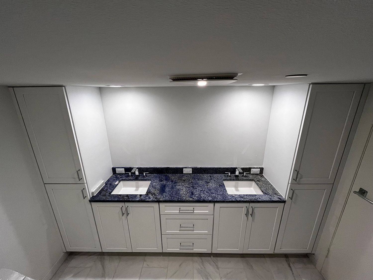Bathroom vanity with two sinks, blue countertop, white cabinets, and built-in lighting.