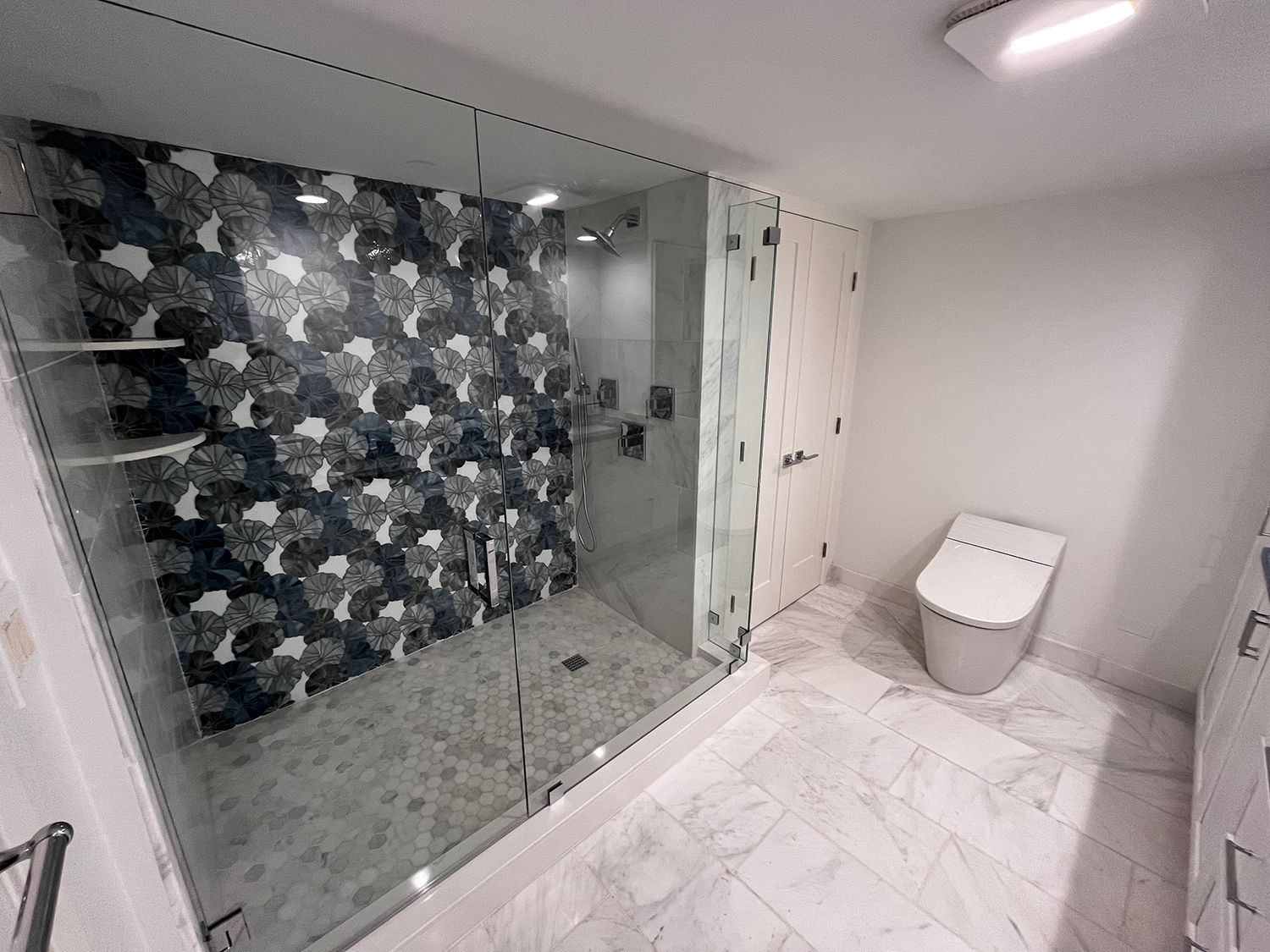 Modern bathroom with patterned shower tile, glass enclosure, and a toilet.
