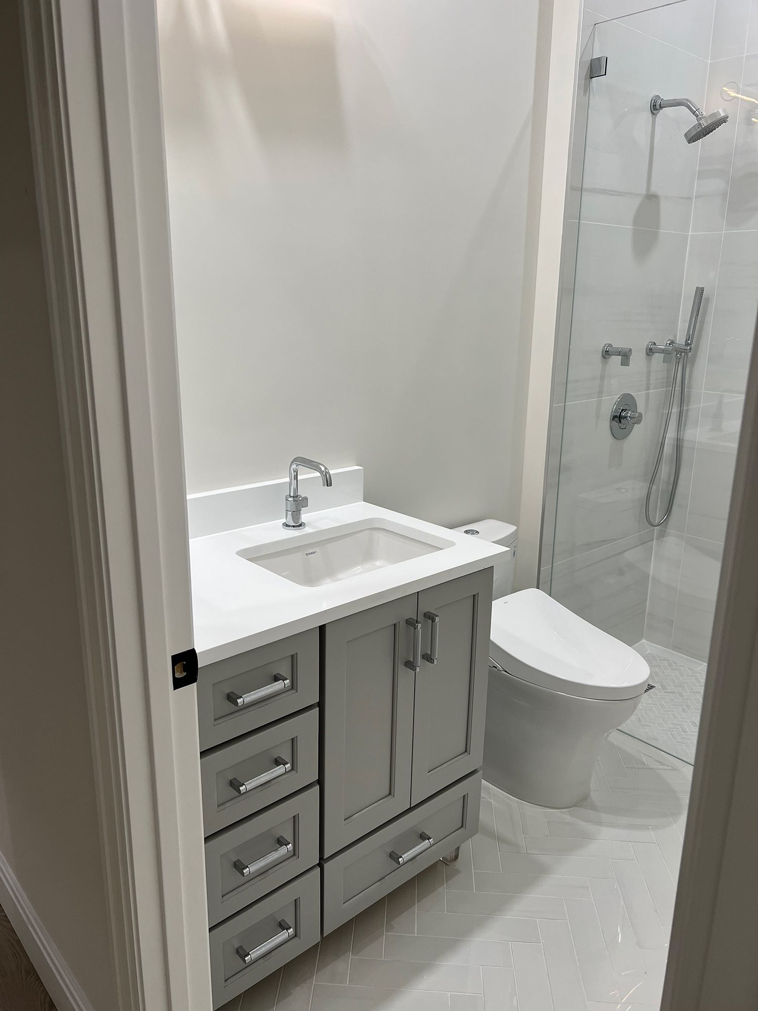 Bathroom with gray vanity, white countertop, toilet, and shower with glass door.