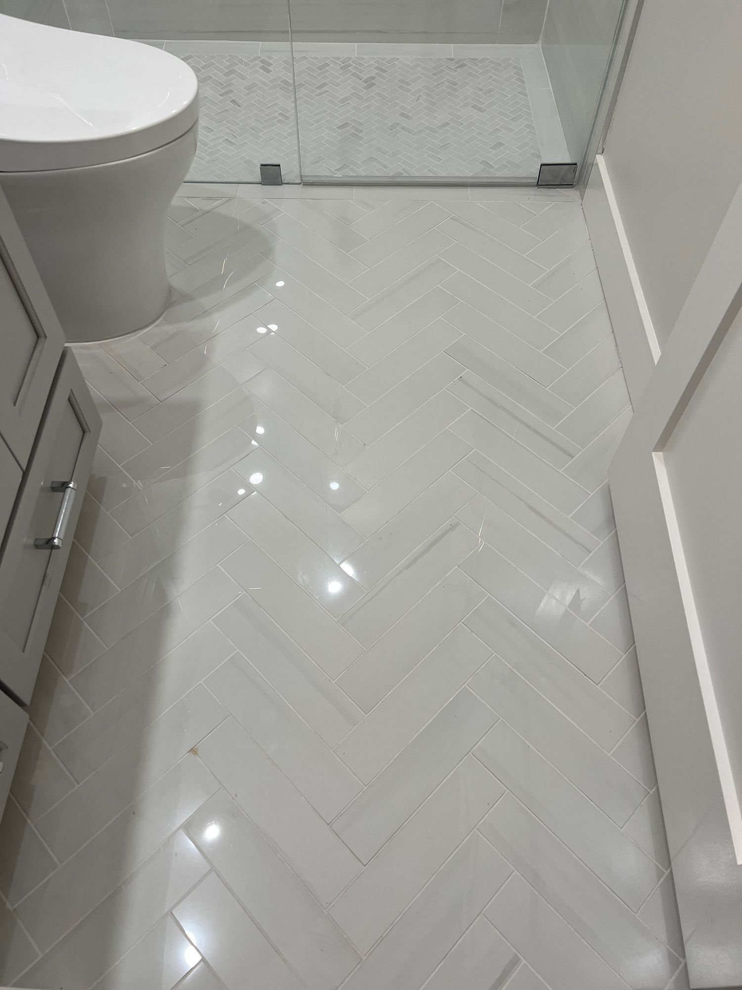 White tiled bathroom floor with water droplets, next to a toilet and a white cabinet.