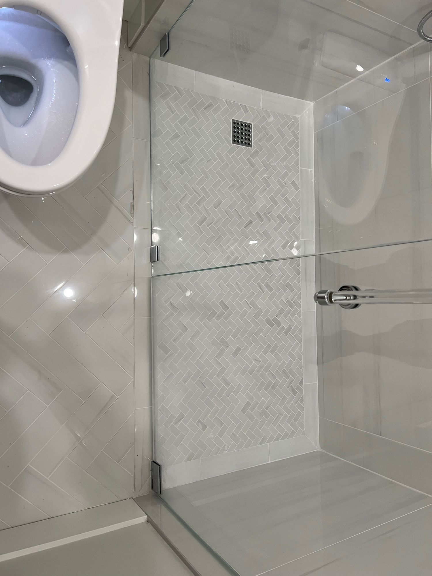 White tiled bathroom with glass shower door, toilet, and patterned shower wall.