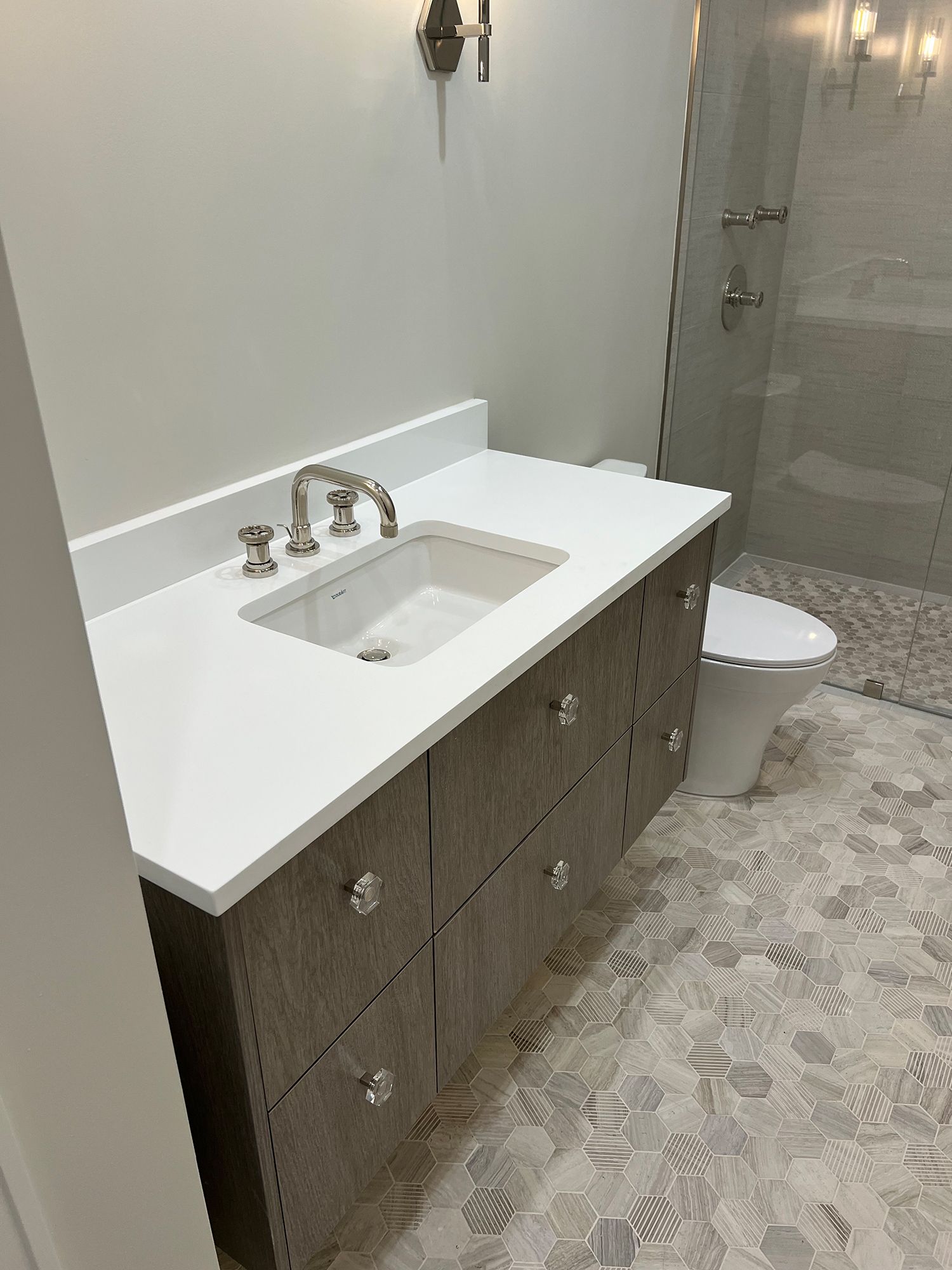 Bathroom with a wood-look vanity, white countertop, sink, toilet, and glass shower.