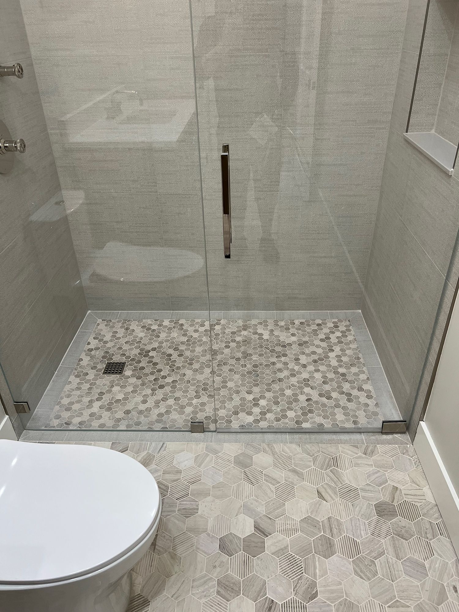 Shower with glass doors and mosaic tile floor, toilet in foreground.