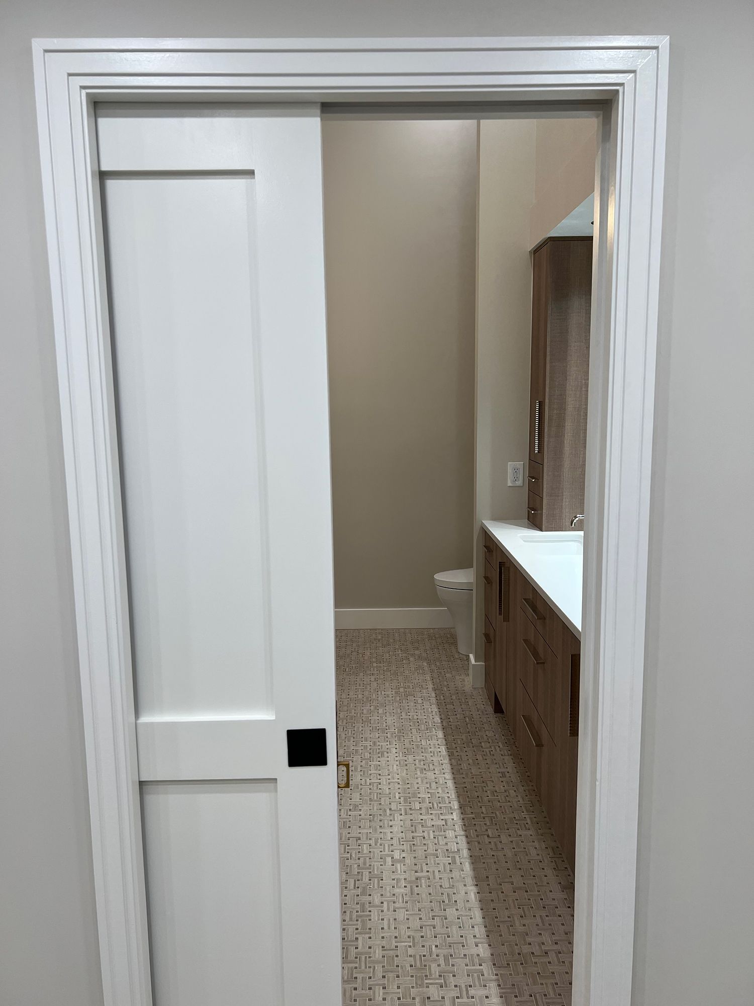 White sliding door partially open to a bathroom with a sink, toilet, and patterned tile floor.