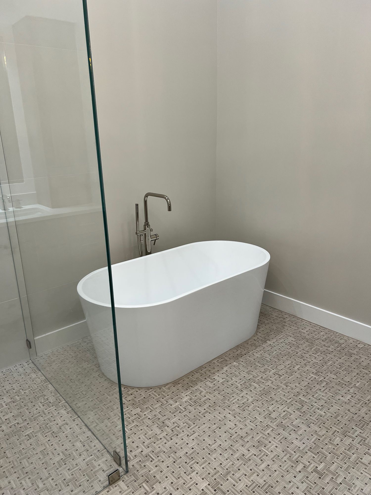 Oval white bathtub in a bathroom, with silver faucet and light-colored tiled floor and walls.