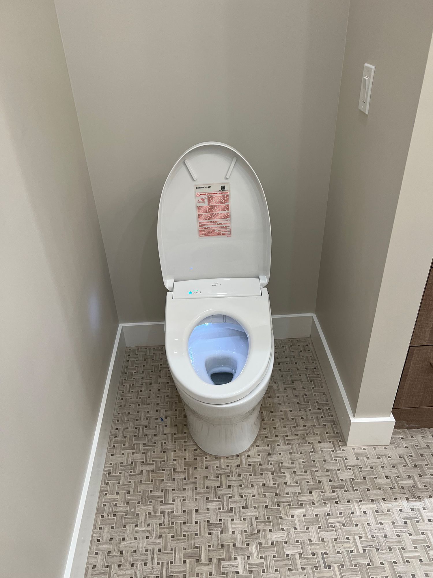 A modern white toilet with the seat up, lit blue, situated in a small corner bathroom.