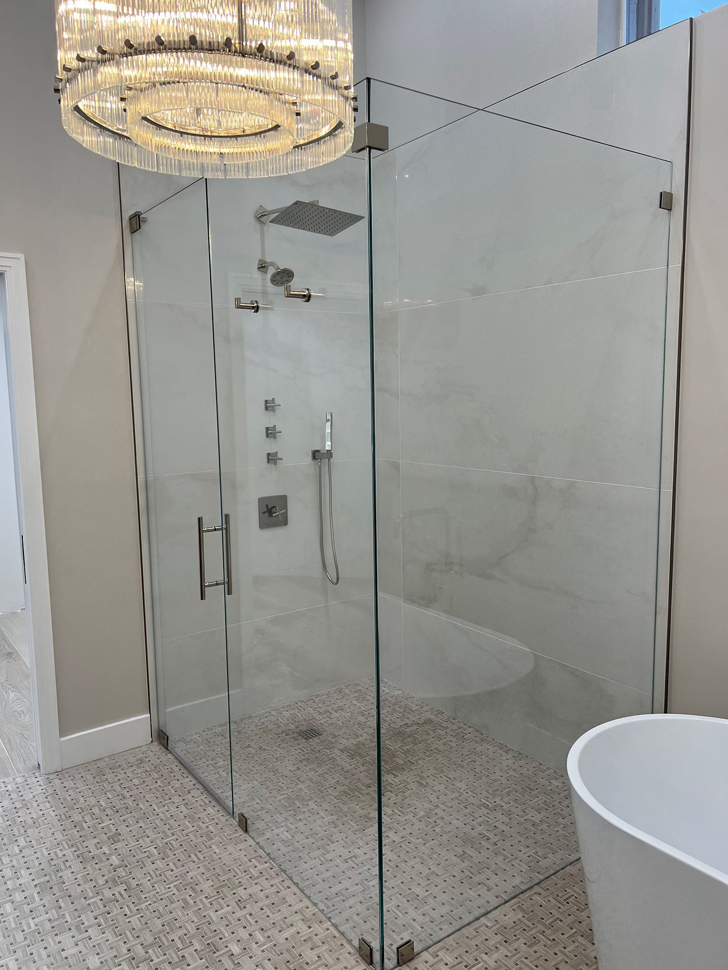 Glass shower enclosure with rain shower head, hand shower, and tiled floor.