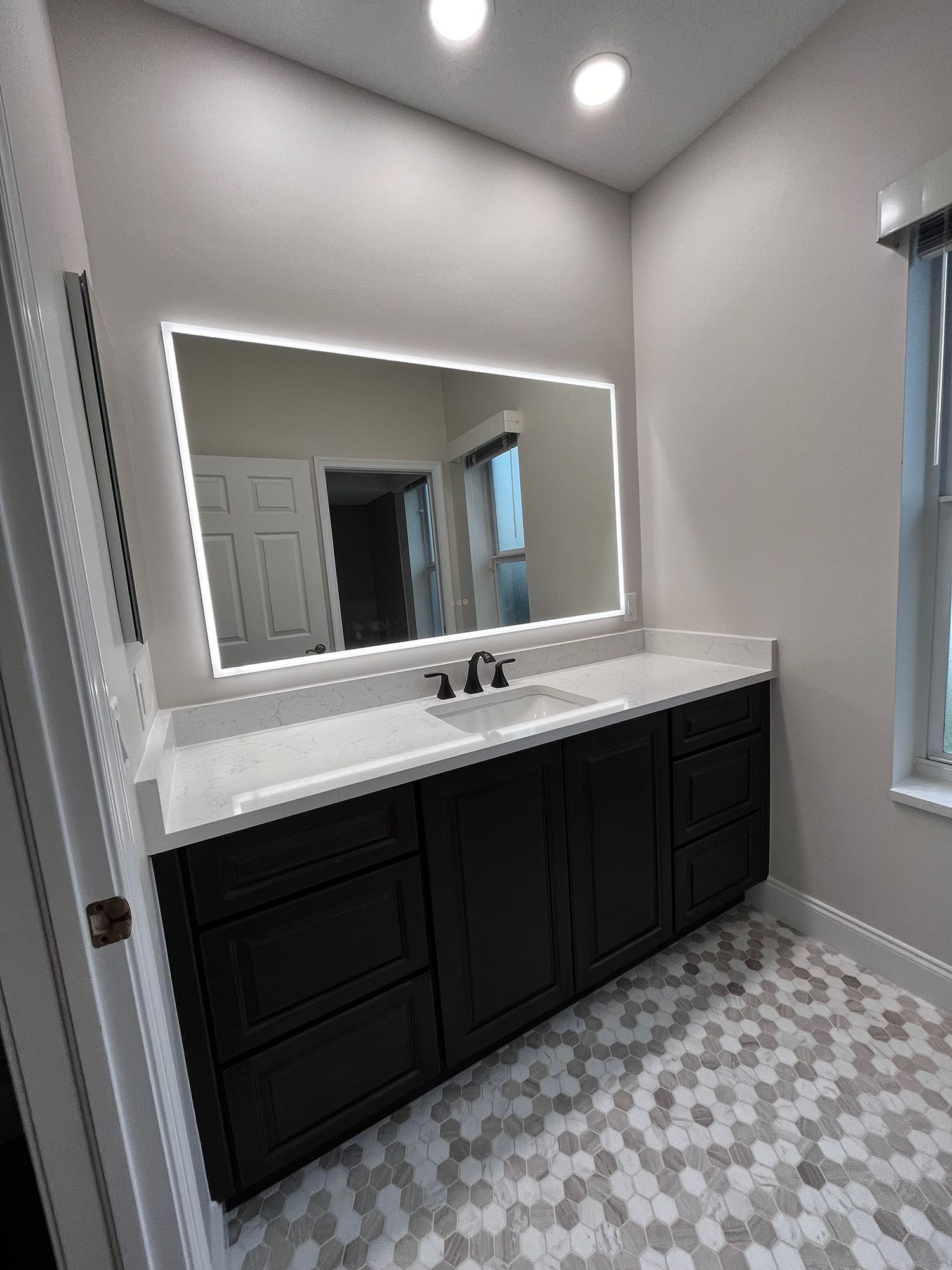 Bathroom with black vanity, white countertop, hexagon tile floor, and illuminated mirror.