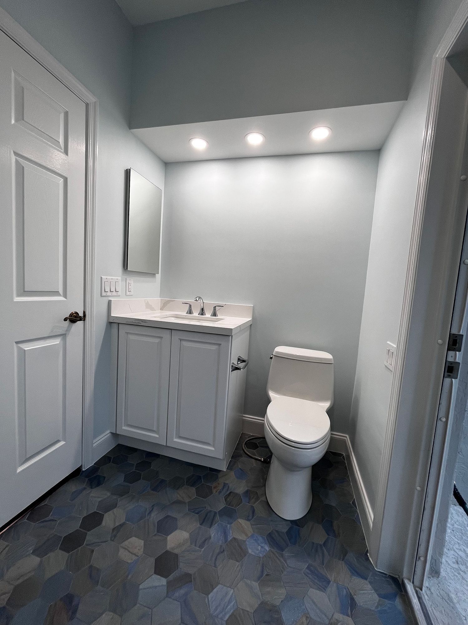 Bathroom with white vanity, toilet, and door; blue hexagon tile floor.