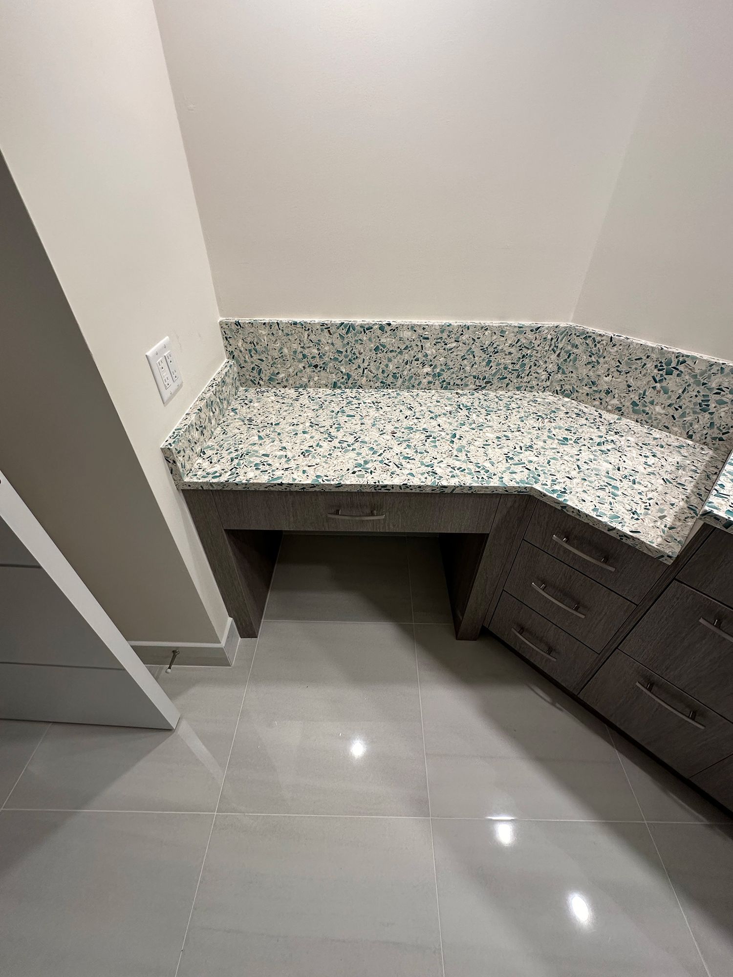 Gray and white speckled countertop on a gray cabinet with drawers. The wall is off-white.
