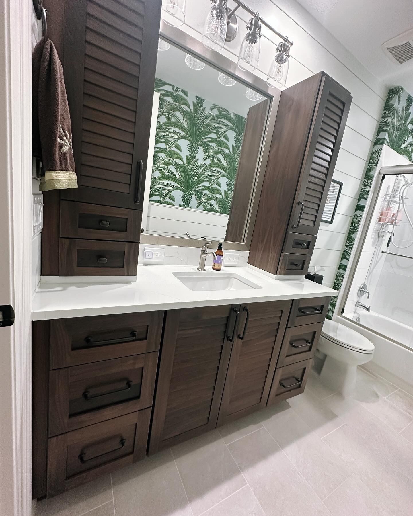 Bathroom with dark brown cabinetry, white countertop, and green palm leaf wallpaper.