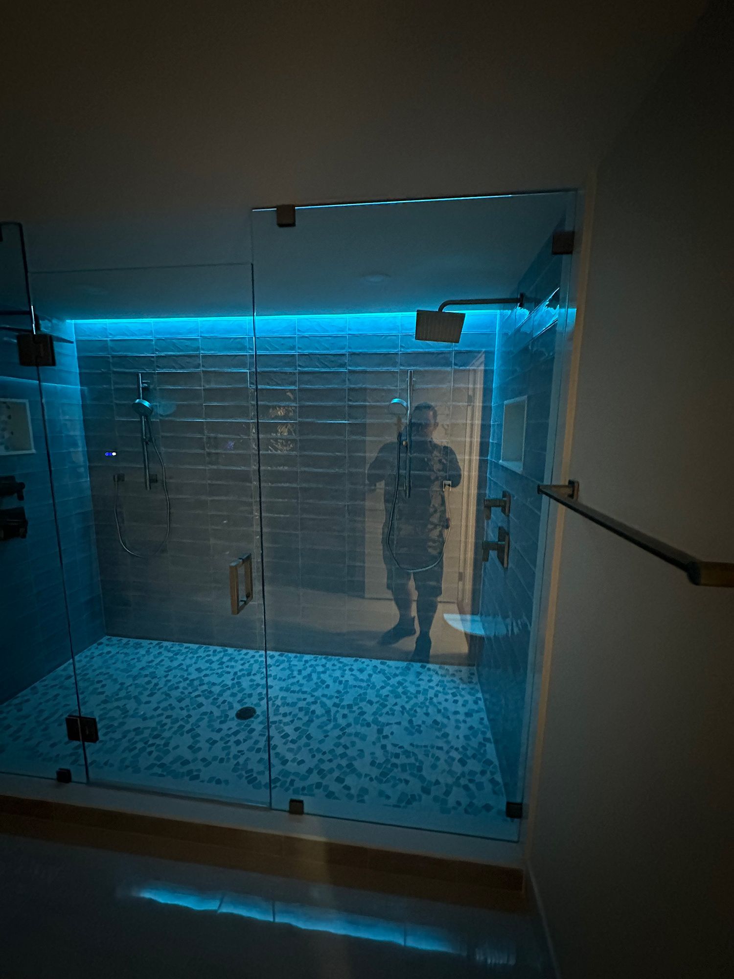 Modern shower with blue-lit ceiling and mosaic tile floor; person visible through glass doors.