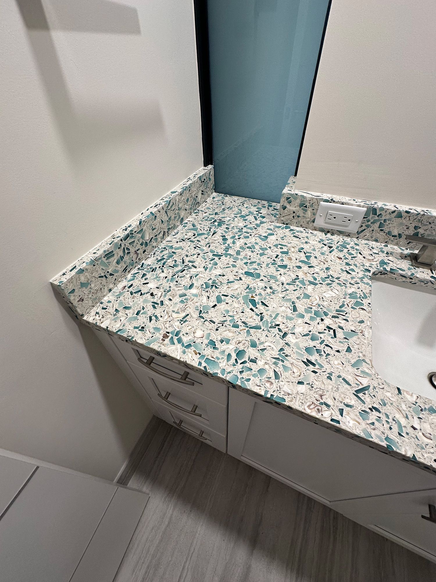 Vanity with turquoise and white speckled countertop and white cabinet.