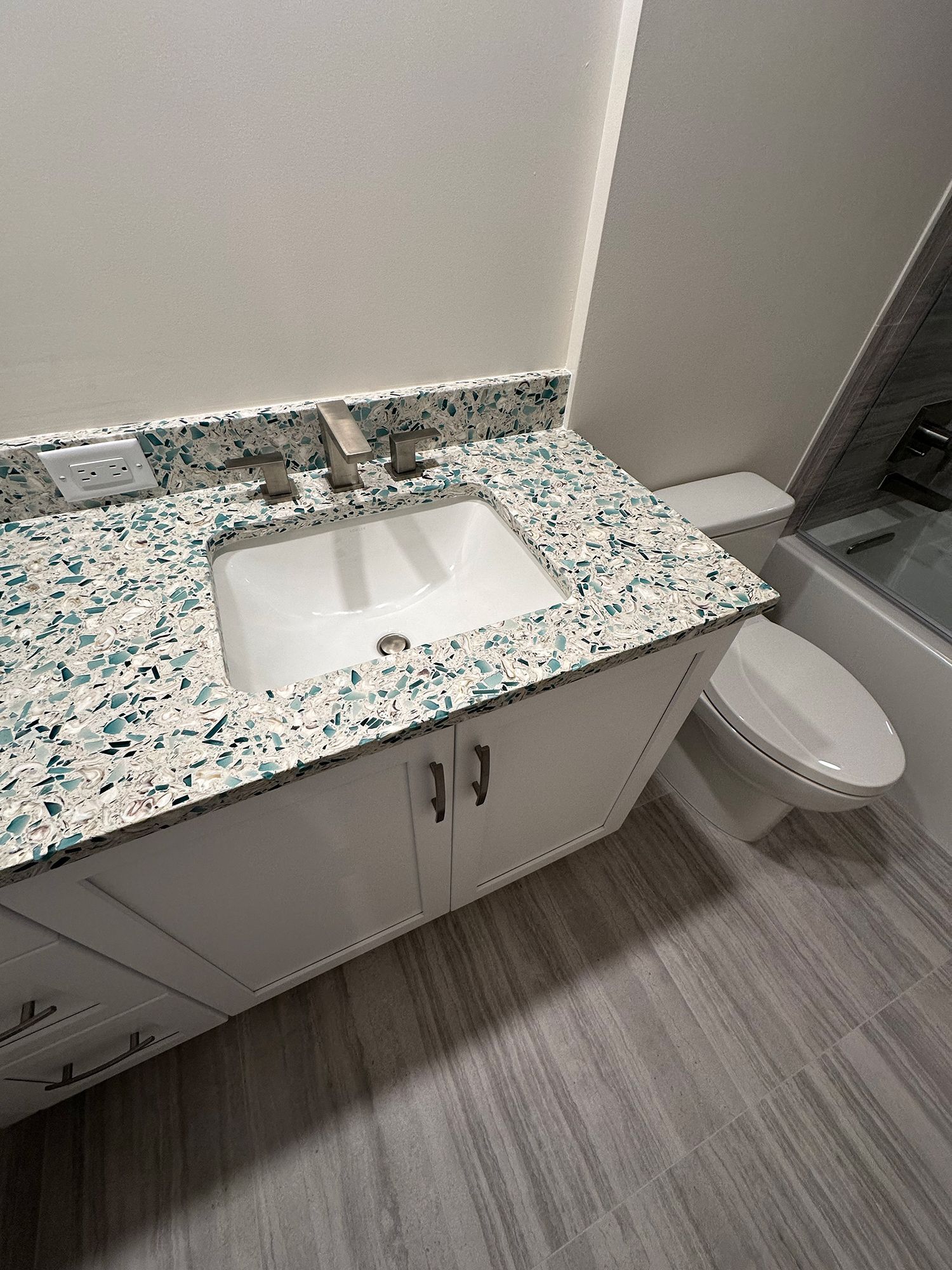 Bathroom vanity with white cabinet, white sink, blue/white countertop, toilet, and gray floor.