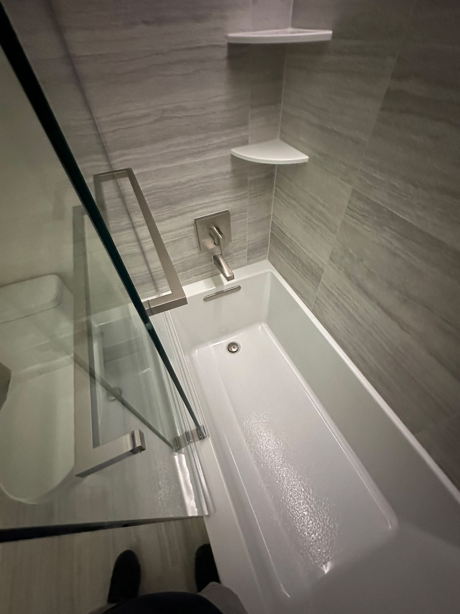 Bathroom with white bathtub, glass shower door, and gray tiled walls.