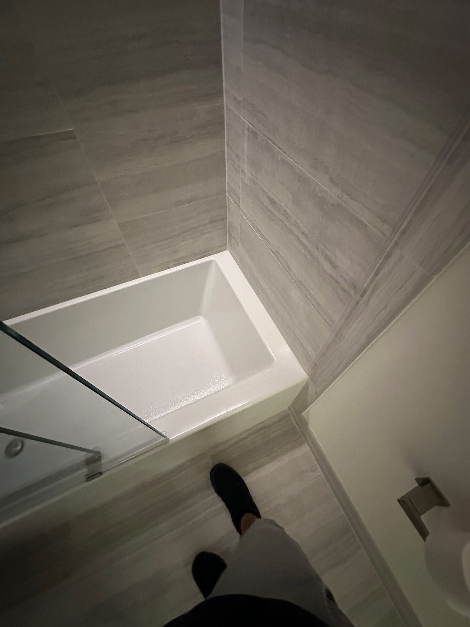 Bathroom with white tub, gray tiled walls, and a glass shower door.