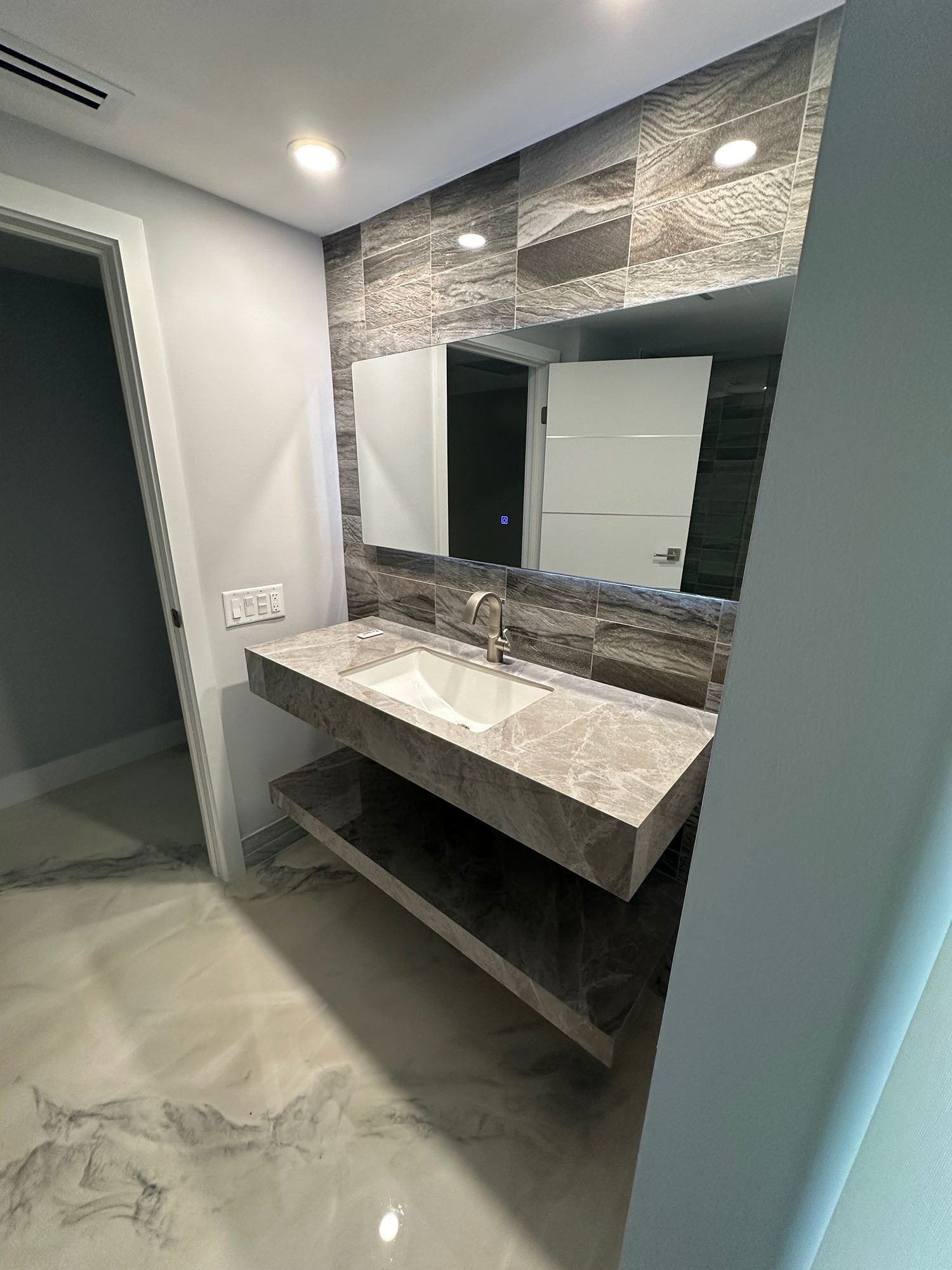 Modern bathroom with floating vanity, marble countertop, stone tile backsplash, and large mirror.
