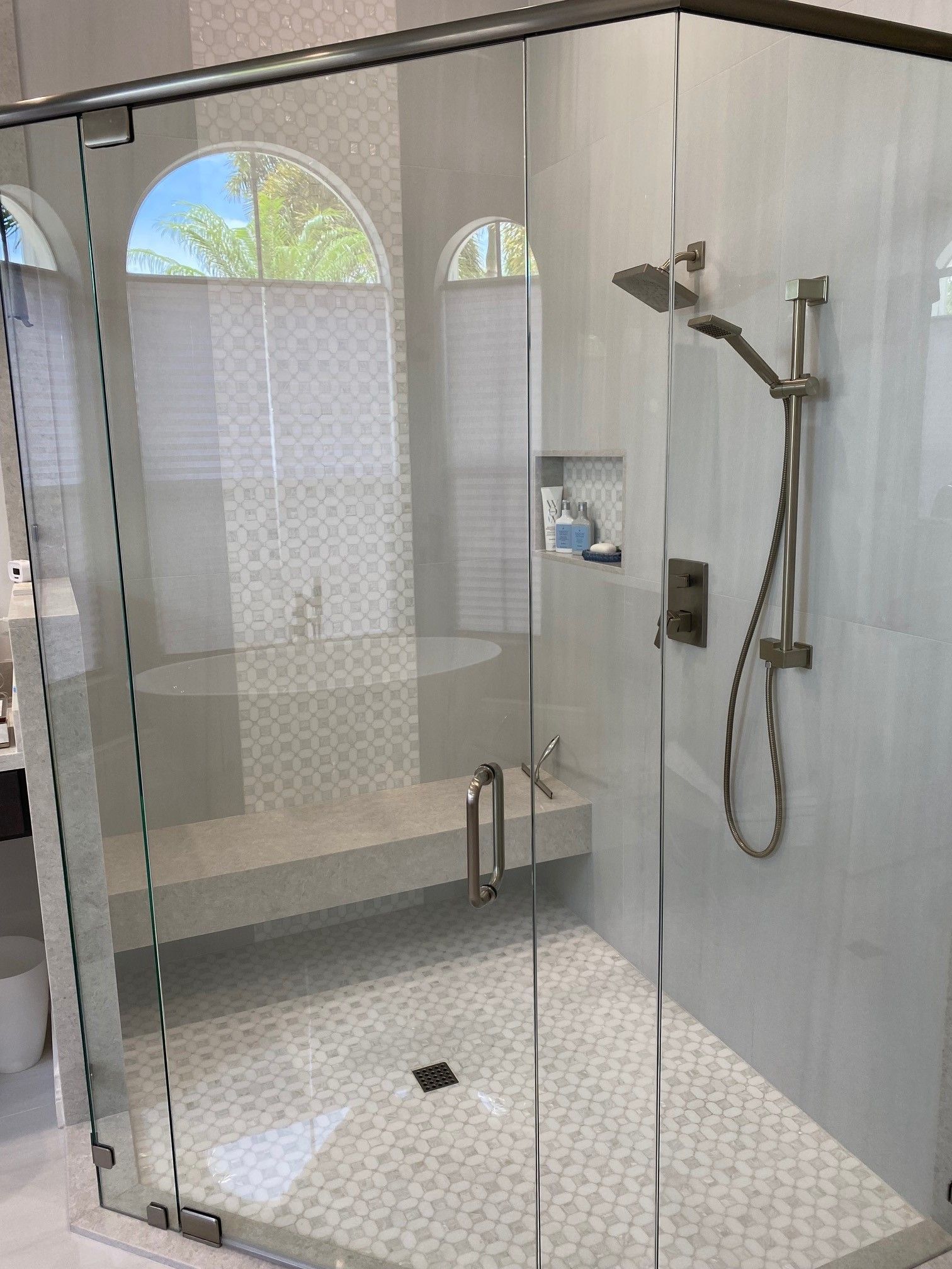 Glass-enclosed shower with white and gray tile, arched windows, built-in bench, and rain shower head.