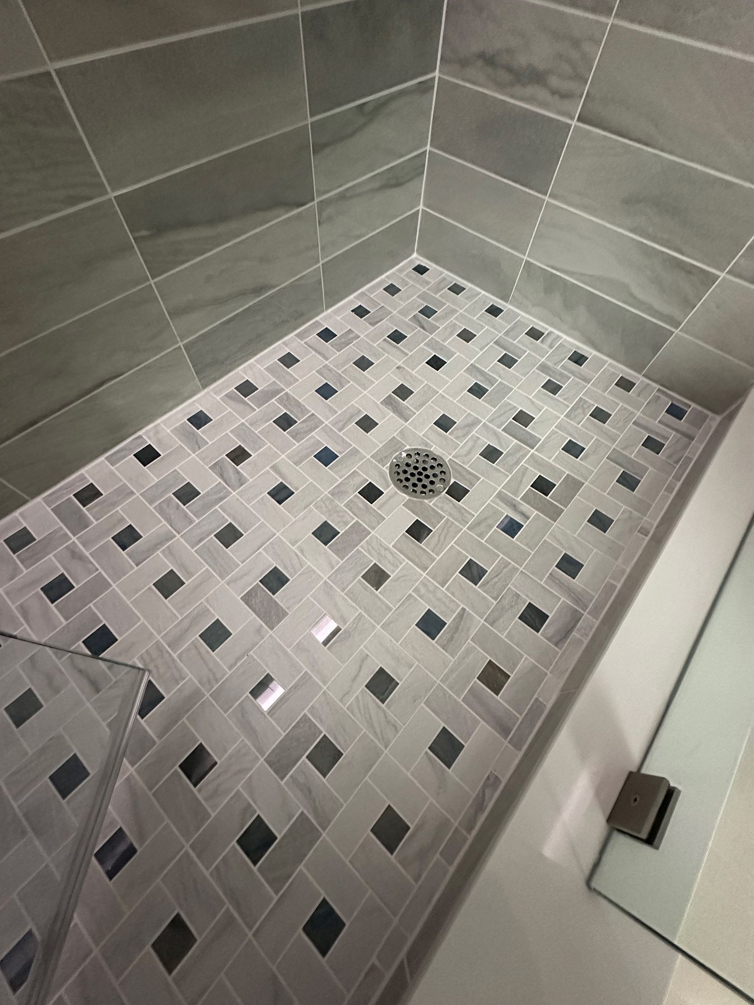 Tiled shower with gray and dark square mosaic floor and large gray wall tiles.