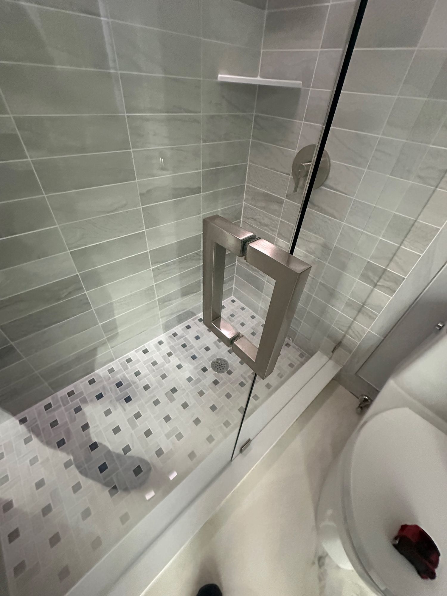 Shower with gray tile walls, glass door, and mosaic tile floor.
