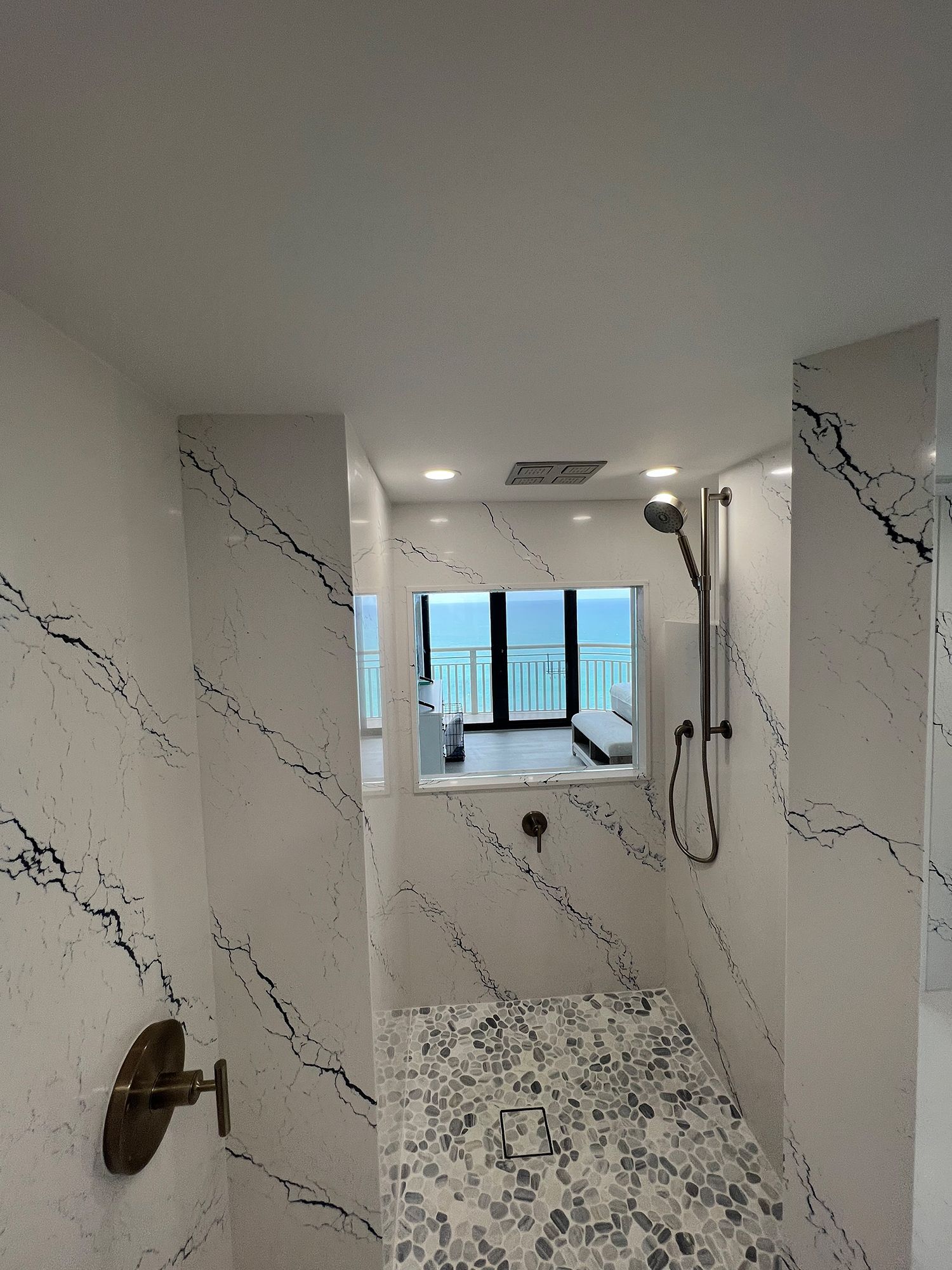 Modern shower with white marble walls and a view through a window.