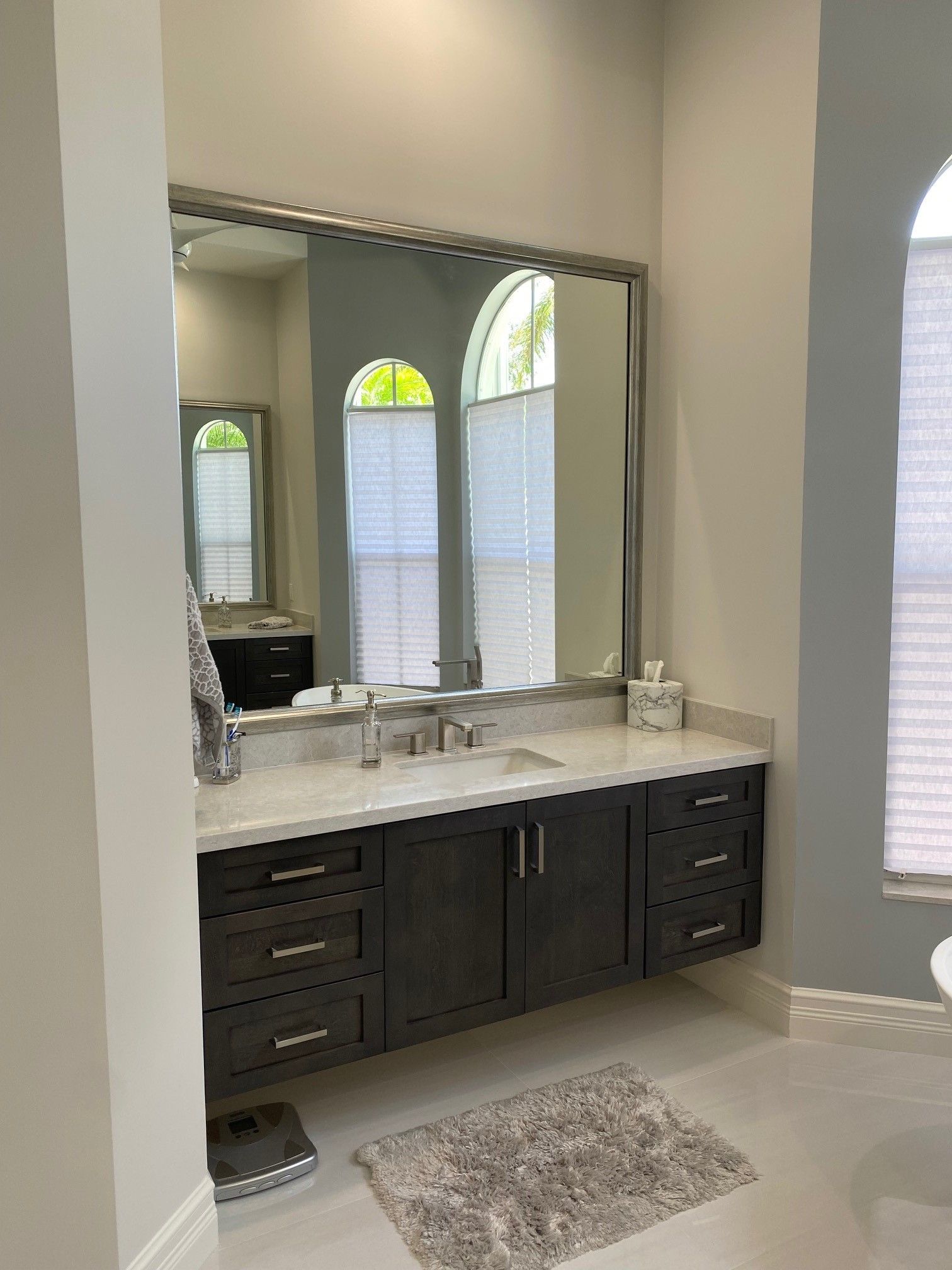 Bathroom with dark gray vanity, large mirror, and arched windows.