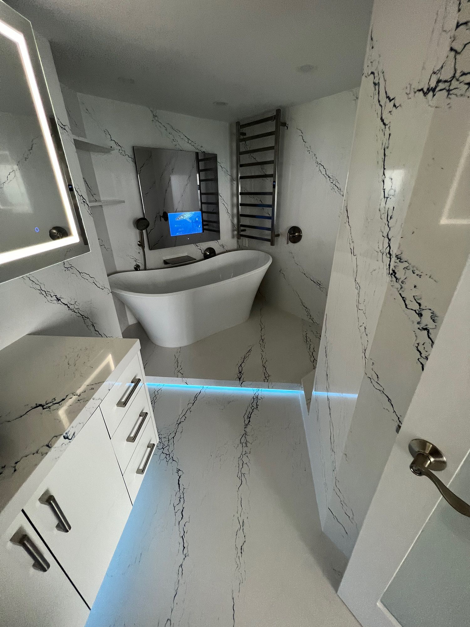 Modern white bathroom with freestanding tub, marble-effect tile, and heated towel rack.