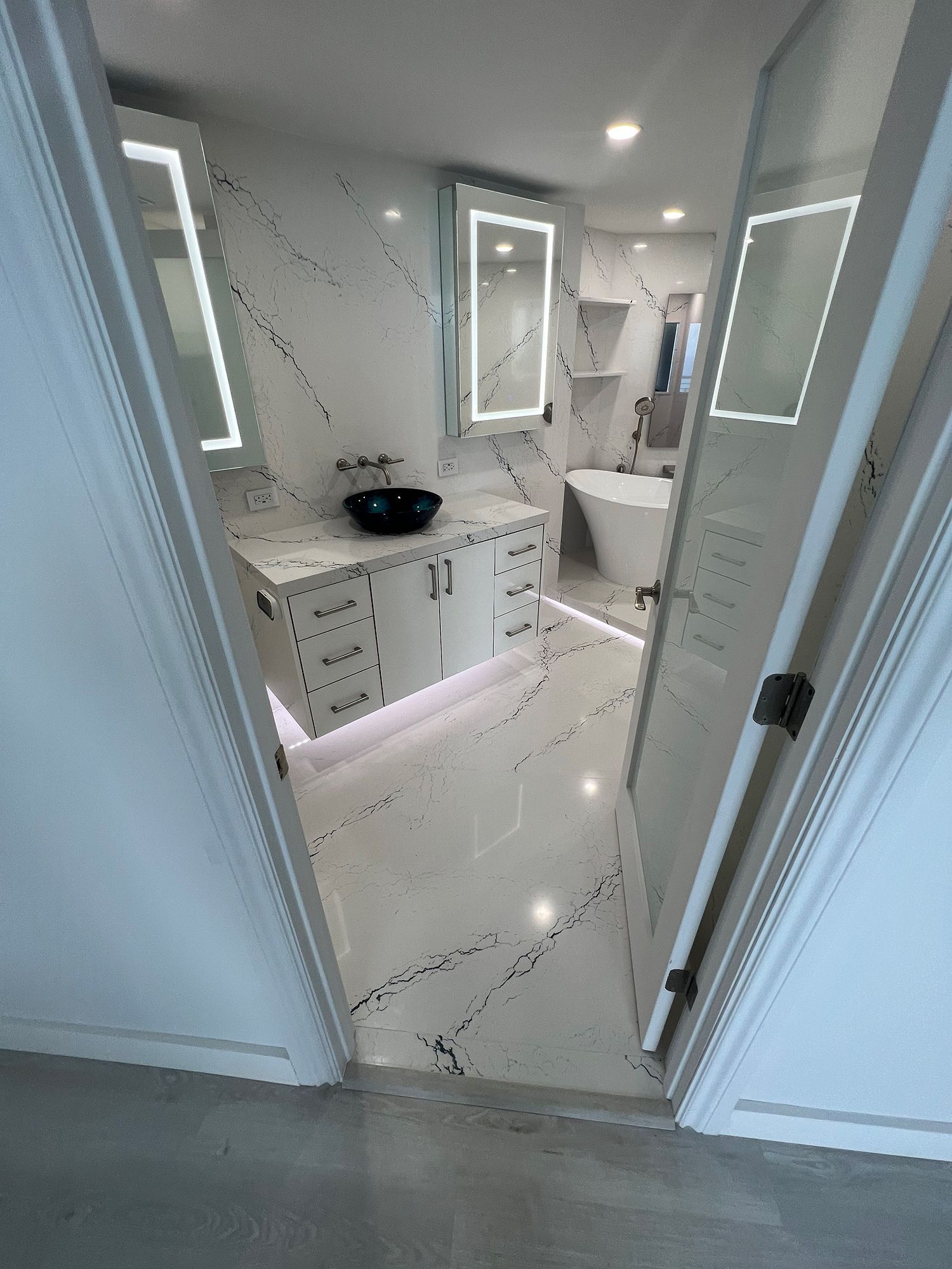 Bathroom with white and black patterned tile, vanity, and backlit mirrors, viewed from a doorway.