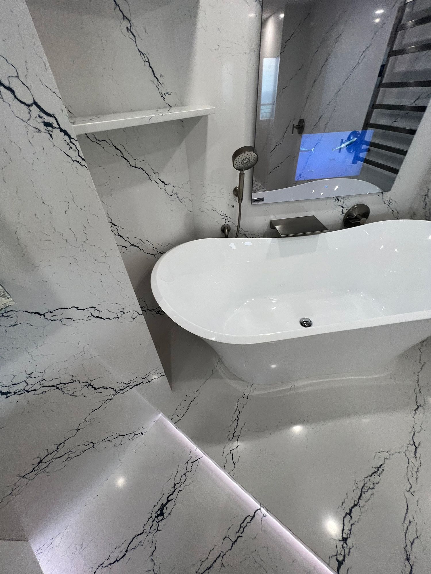 White marble bathroom with freestanding tub, shower, and shelf. Black veining in the marble.