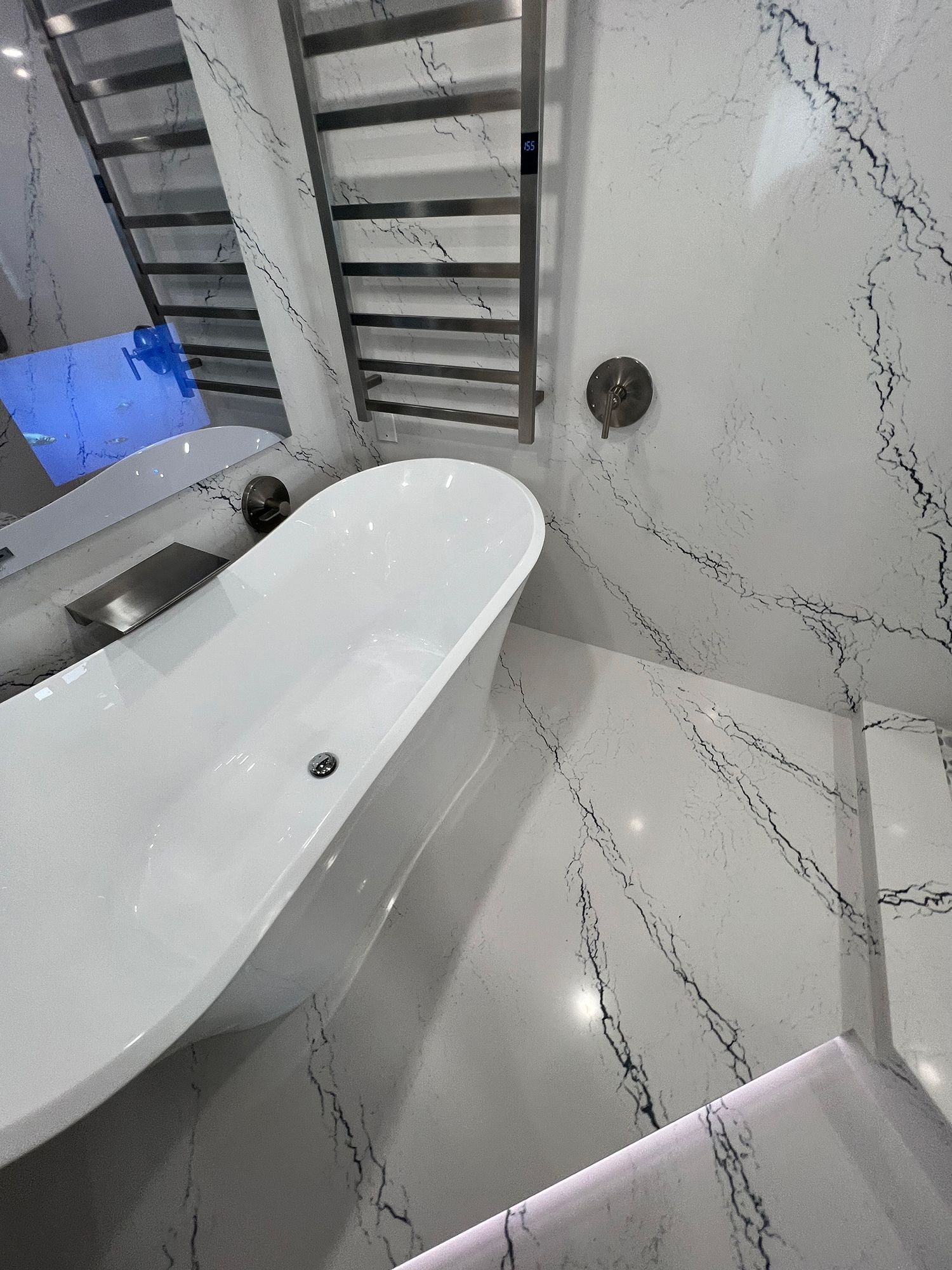 Modern bathroom with white freestanding tub, marble-effect walls, and heated towel rack.