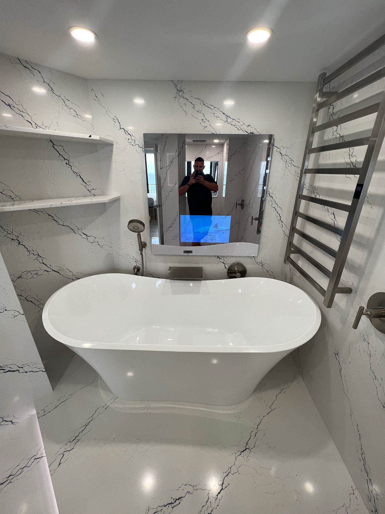 Luxurious white bathroom with a freestanding tub, heated towel rack, and marble-like walls.