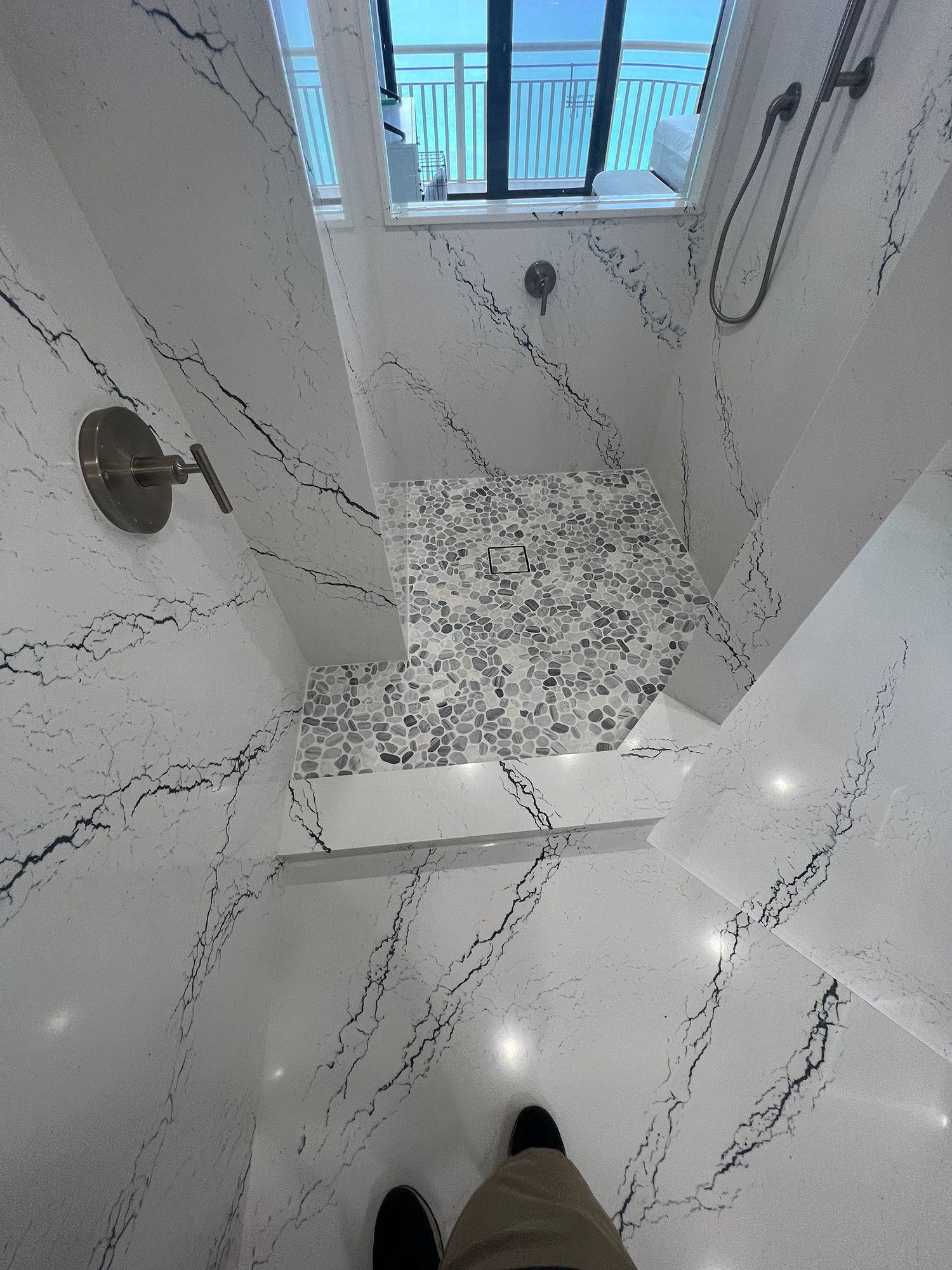 White marble shower with black veining, patterned tile floor, window.