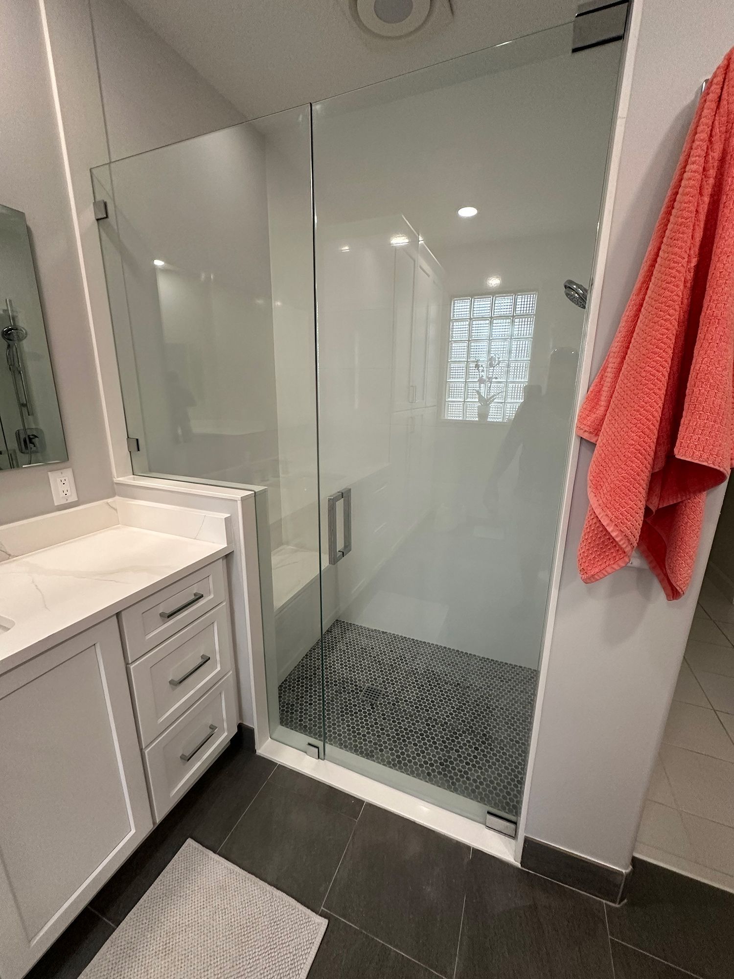 Modern bathroom with glass shower, white vanity, and coral towel. Gray stone floor and tiles.
