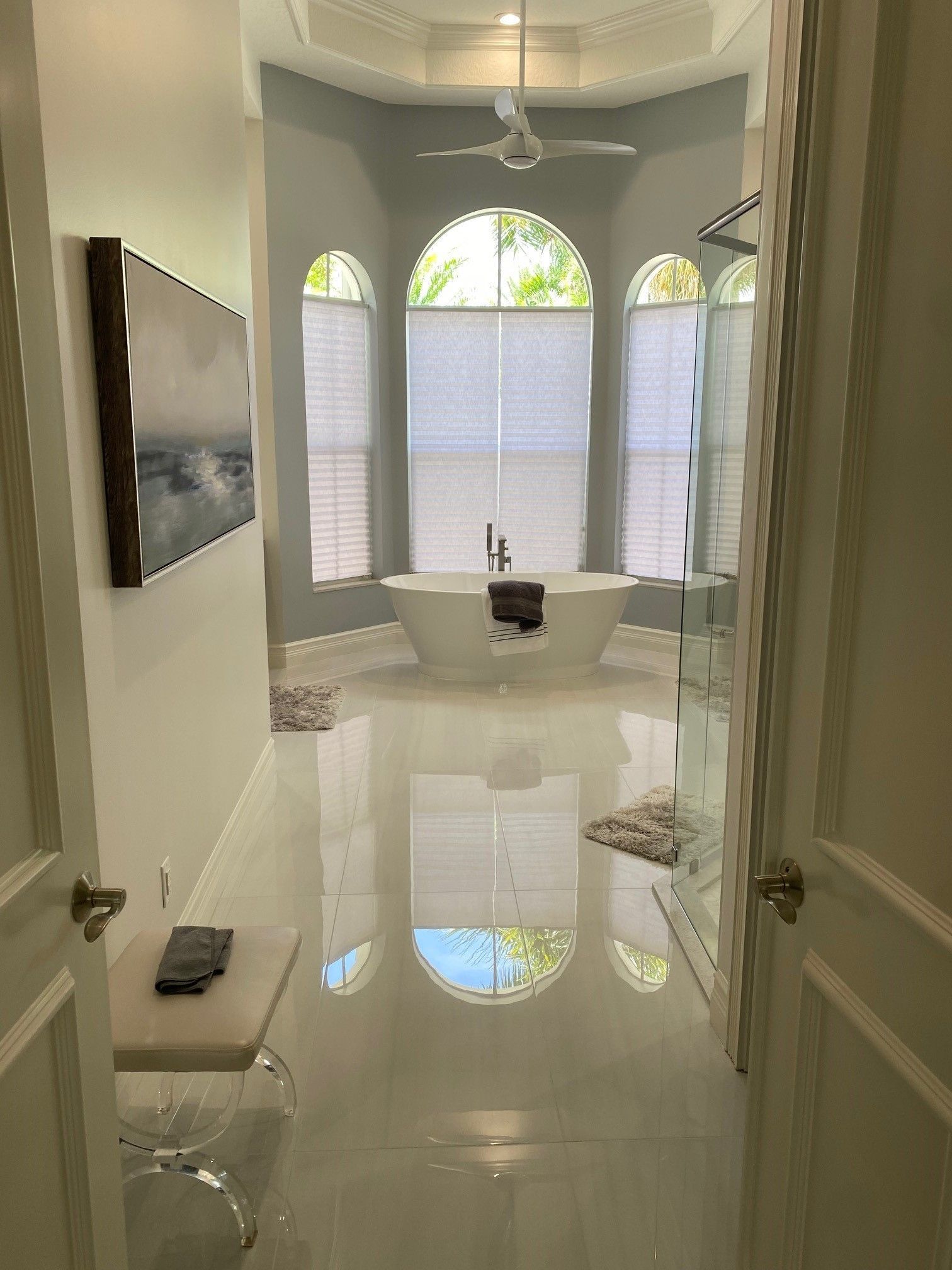 Spacious bathroom with soaking tub, arched windows, and white tile floor.