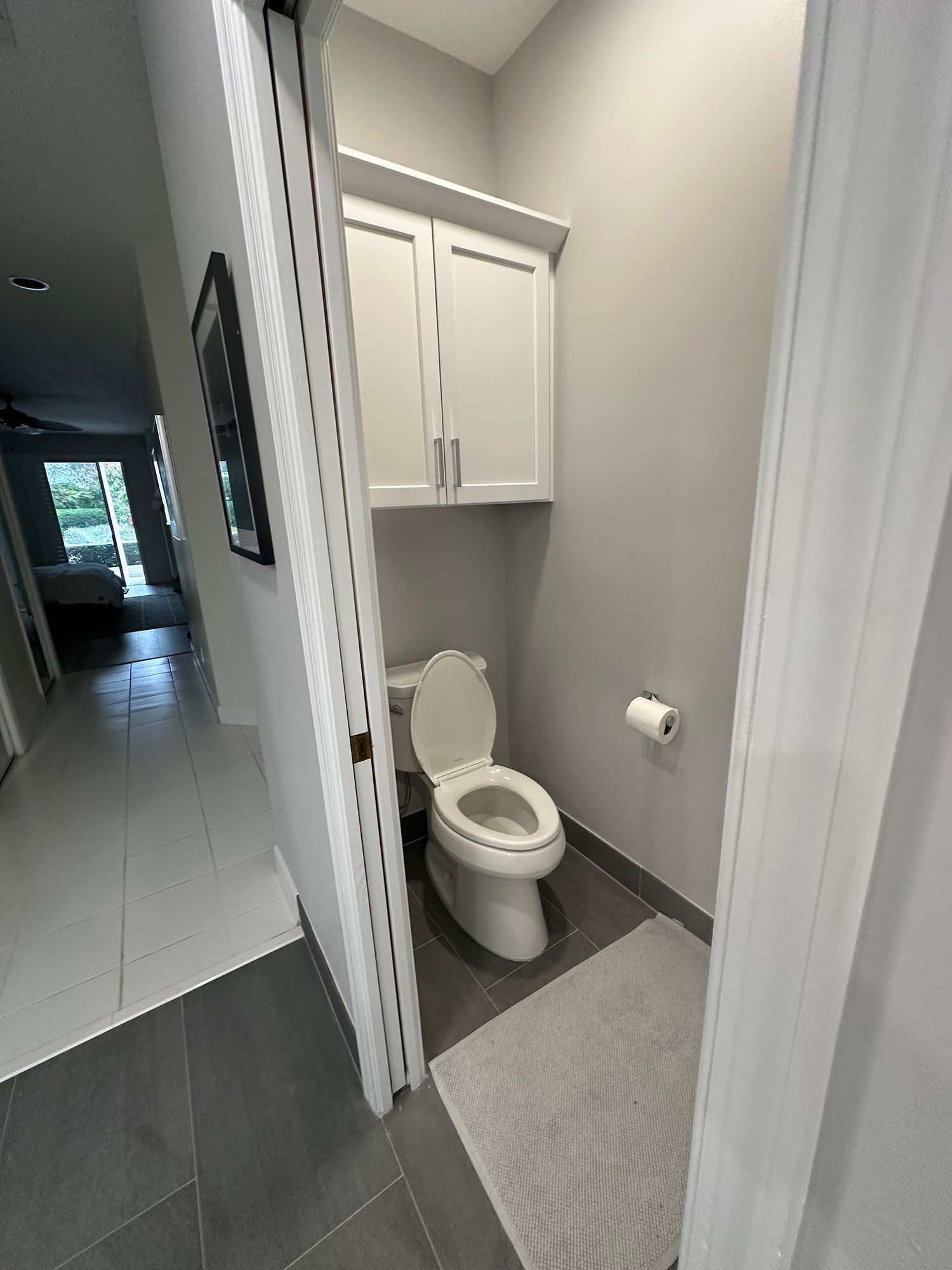 Small bathroom with a toilet, overhead cabinet, and gray walls and floor.