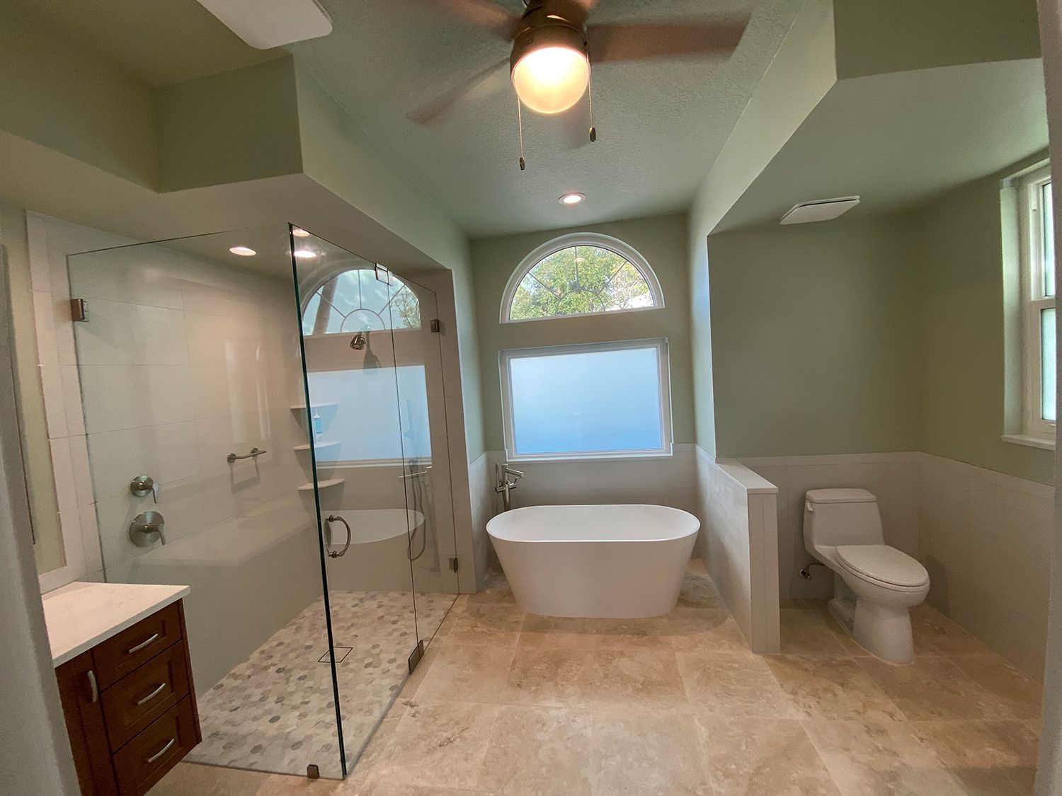 Spacious bathroom with white tub, walk-in shower, and toilet, light green walls, beige tile floor.