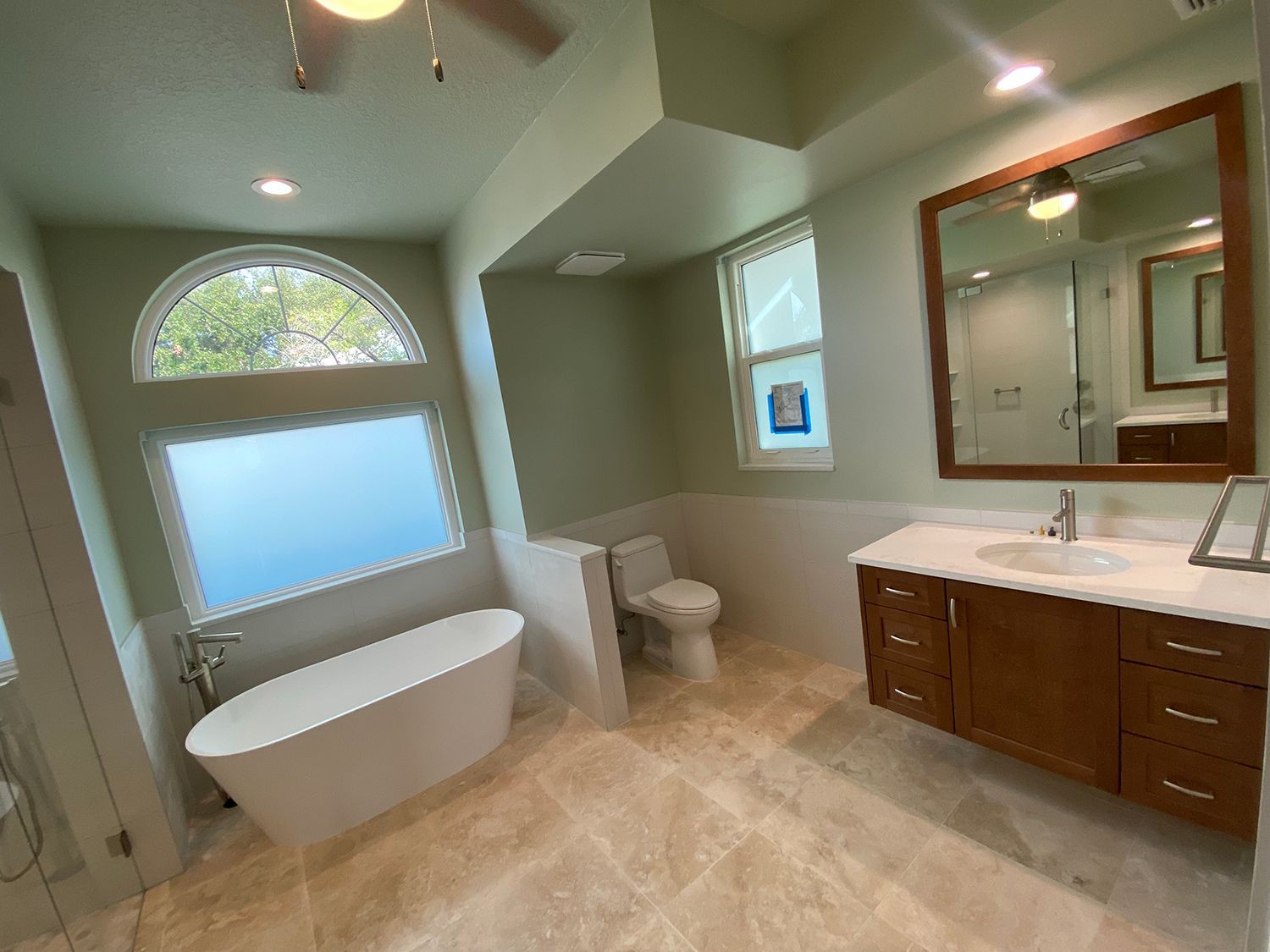 Spacious bathroom with a white tub, toilet, and vanity. Beige tile floor and light green walls.