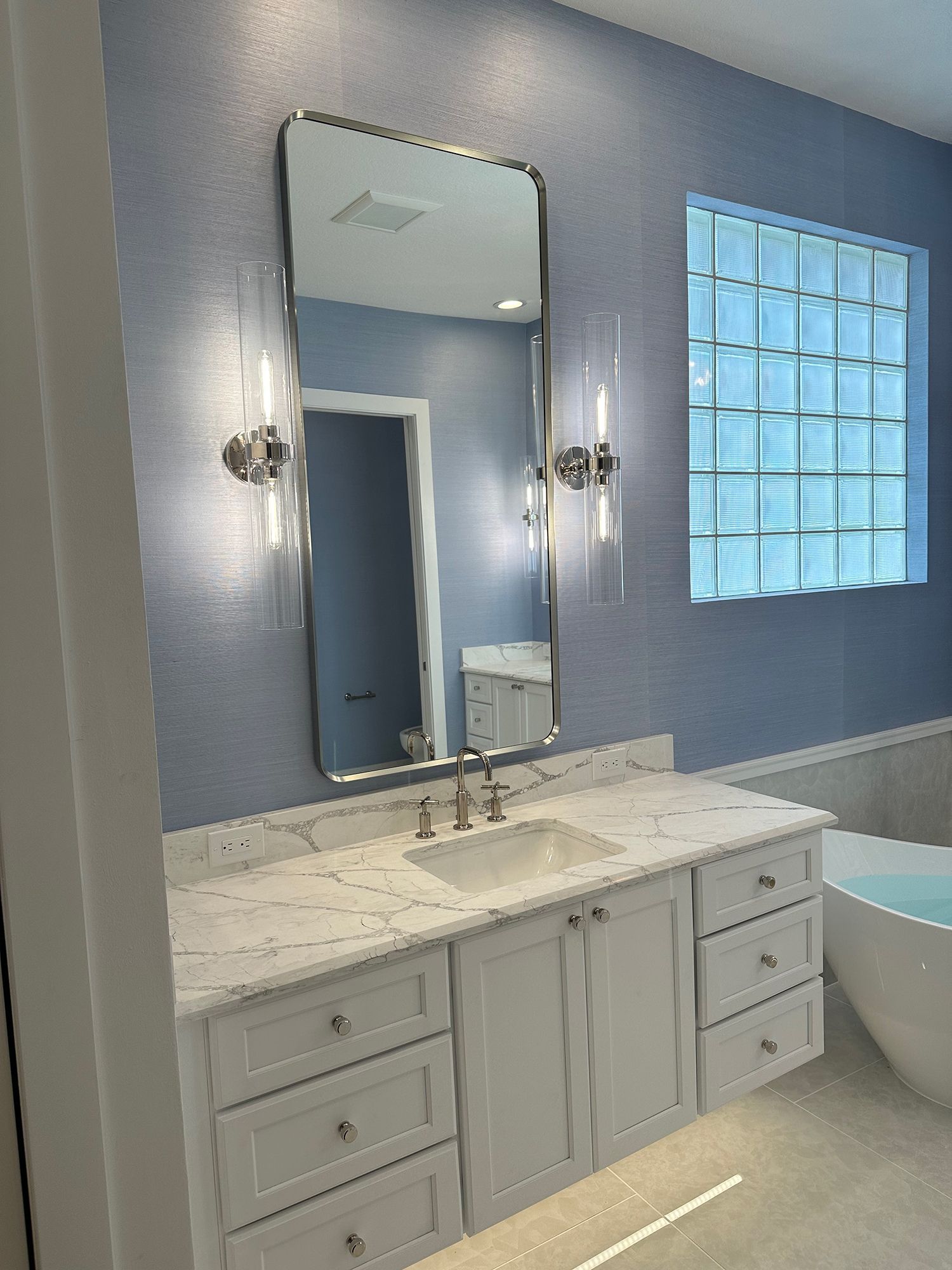 Bathroom with a white vanity, marble countertop, large mirror, and blue textured walls.