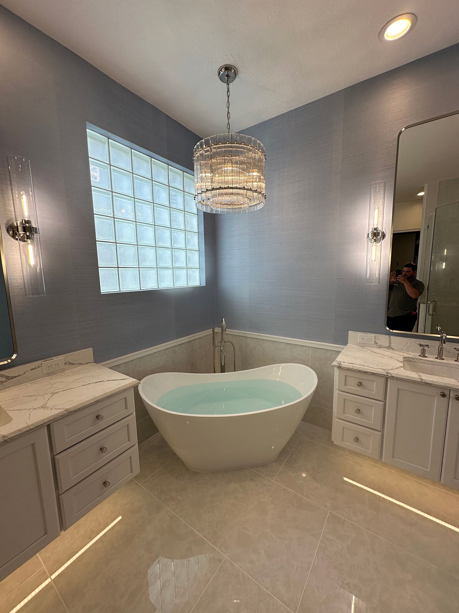 Elegant bathroom with a free-standing tub, marble countertops, glass brick window, and a chandelier.