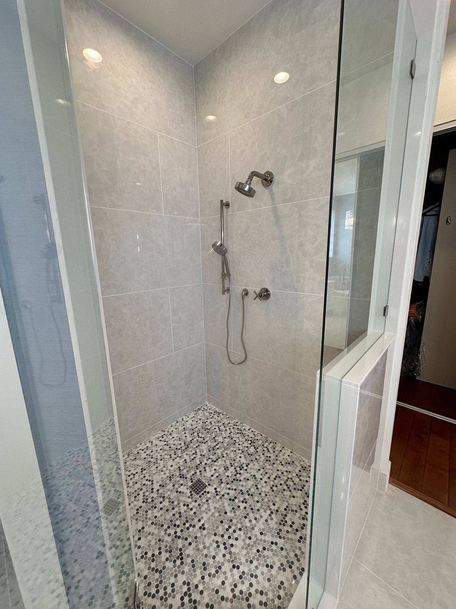 Shower with light gray tiled walls, pebble floor, and glass door.