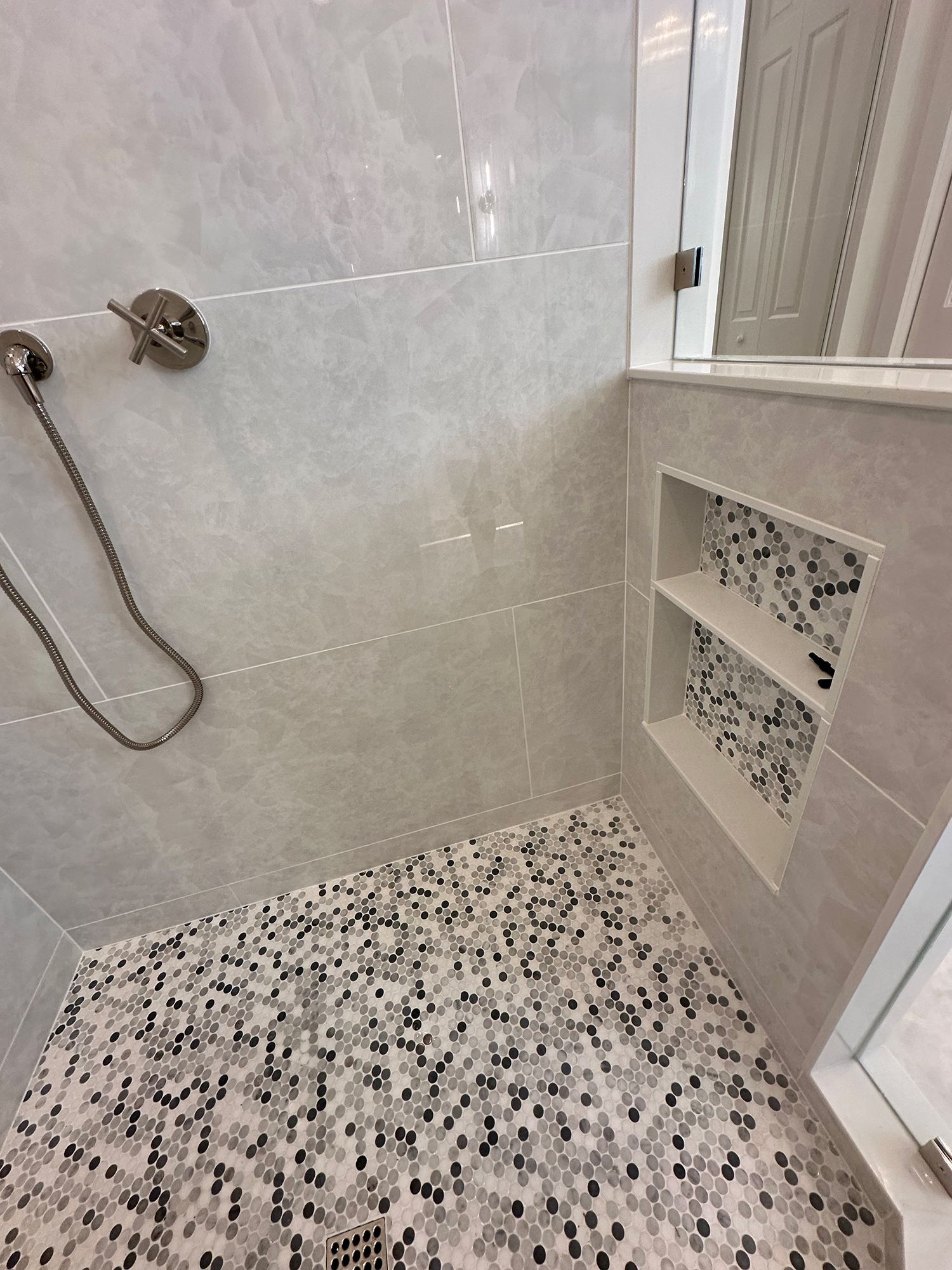Shower interior with gray marbled walls, mosaic floor, and built-in shelf.