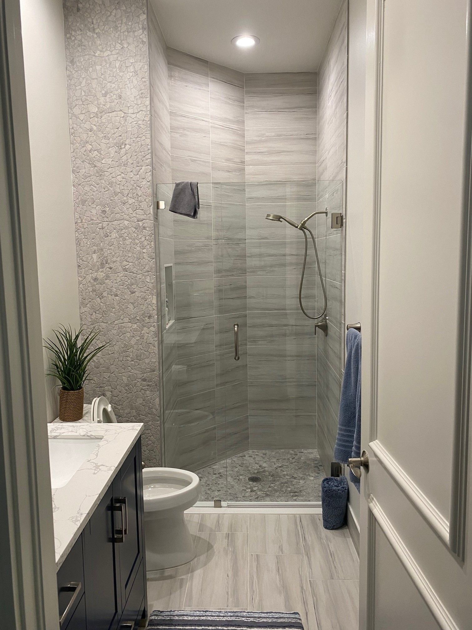 Bathroom with gray and white tile, shower, vanity, toilet, and blue accents.