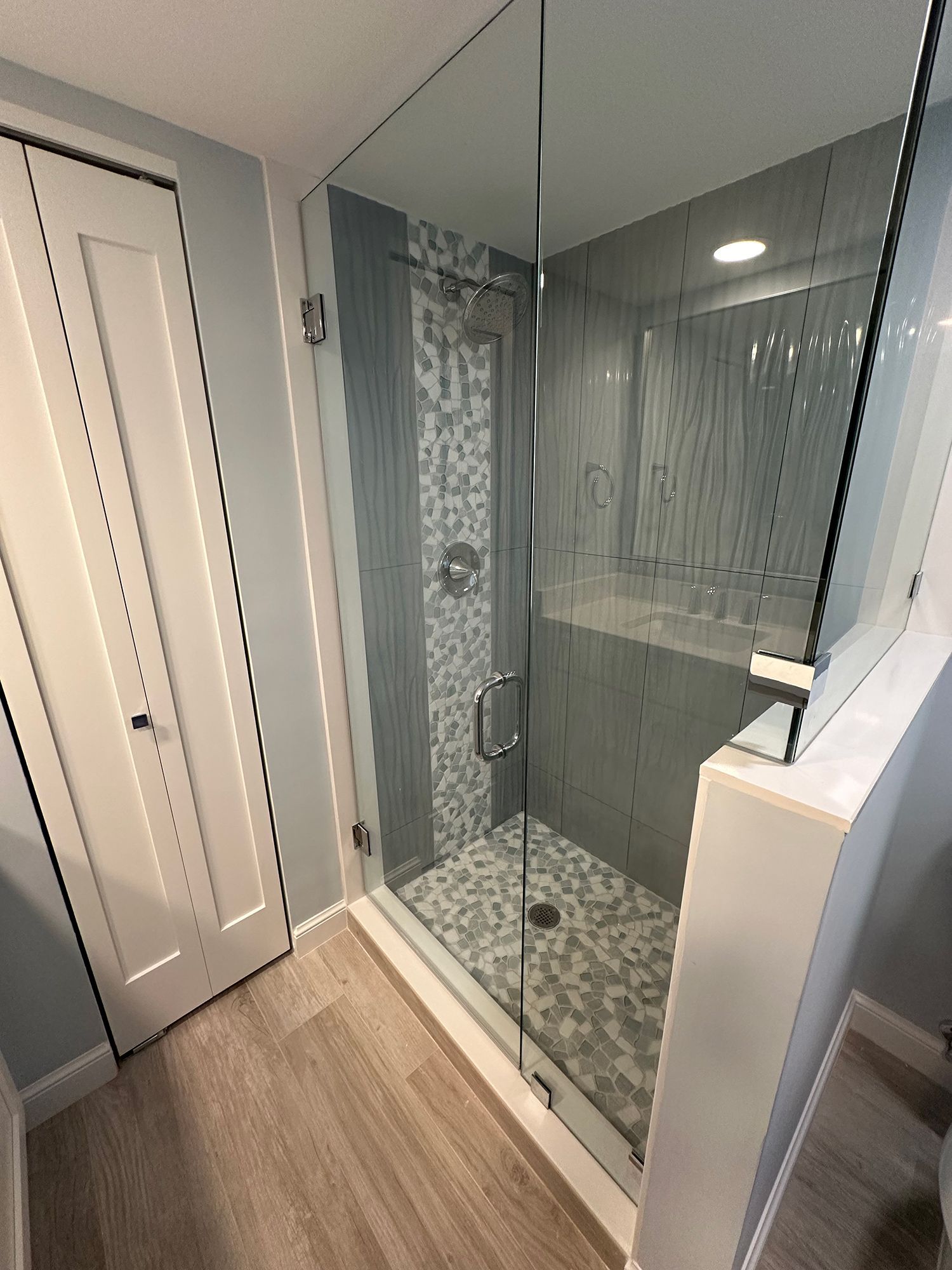 Modern bathroom with glass shower enclosure, light blue walls, and patterned tile.