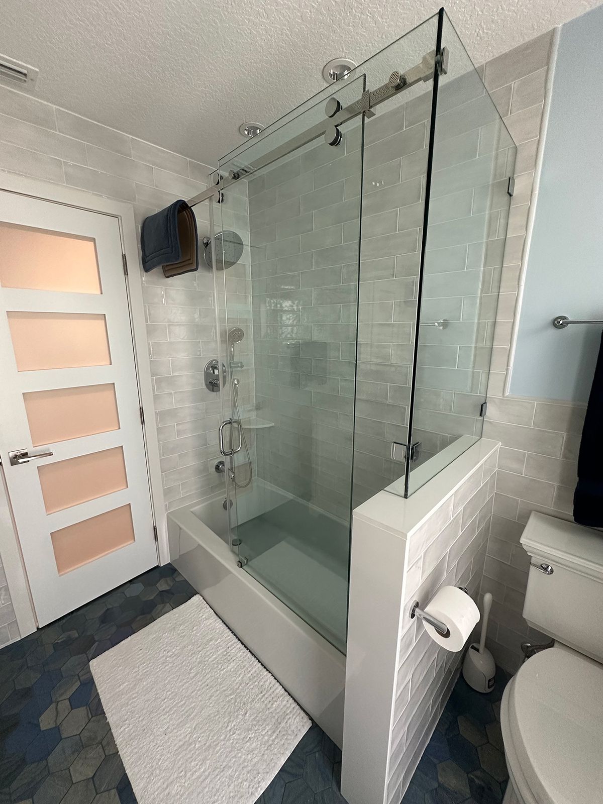 Bathroom with glass shower doors, white subway tile, a bathtub, and a toilet.