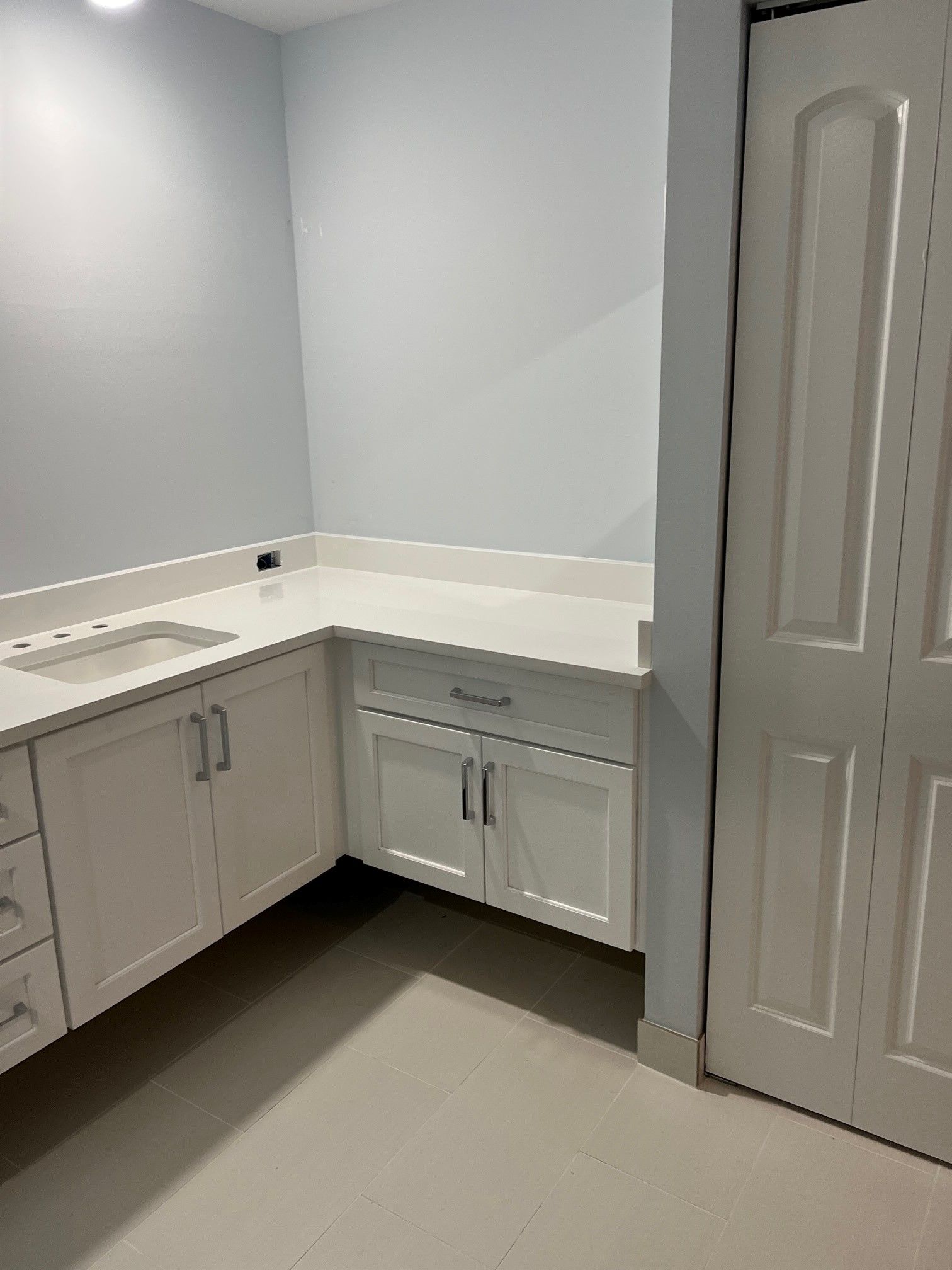 White bathroom vanity with sink and cabinets, light blue walls, and a white door.