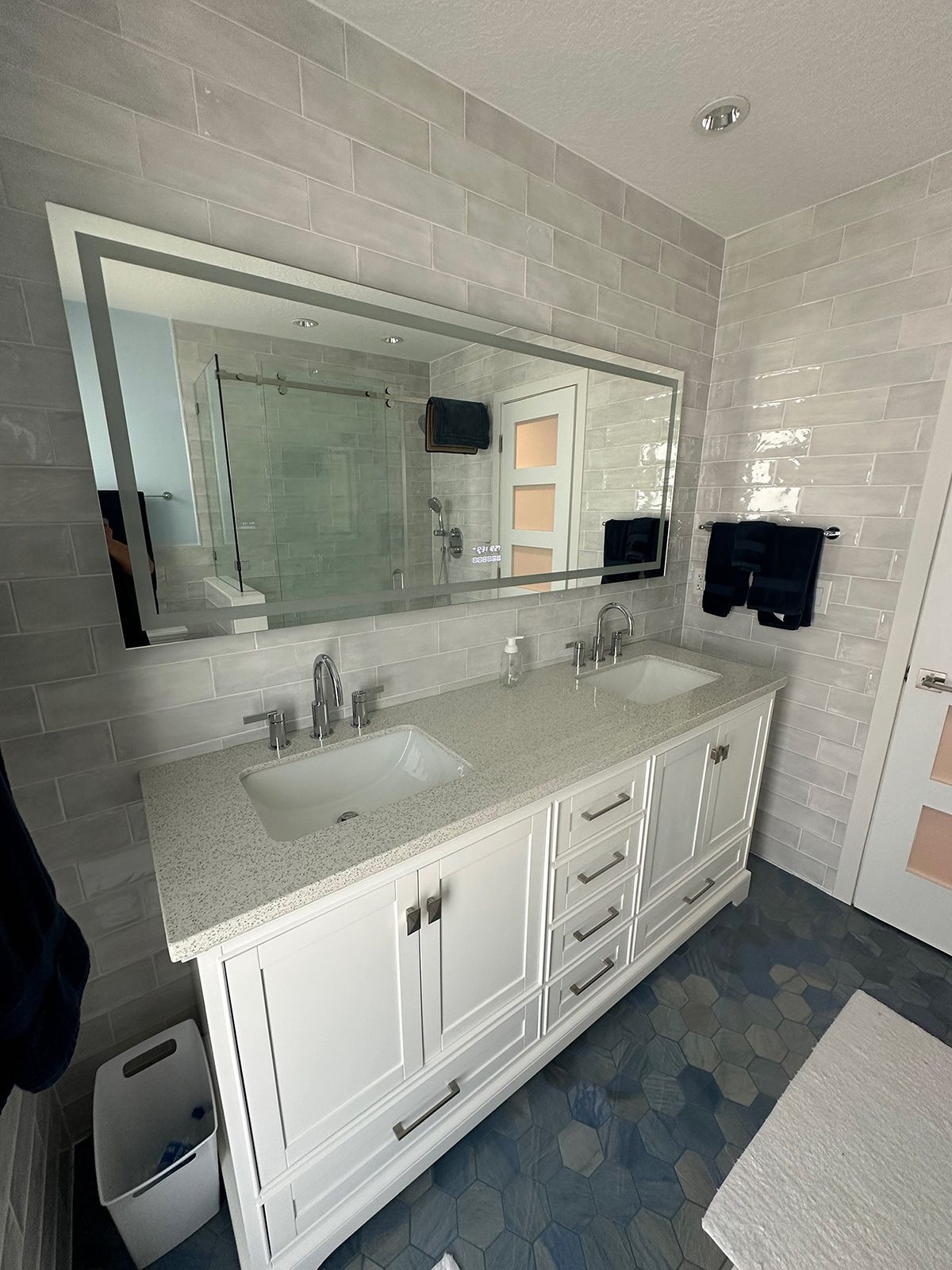 Bathroom with white vanity, double sinks, large mirror, and blue tiled floor.