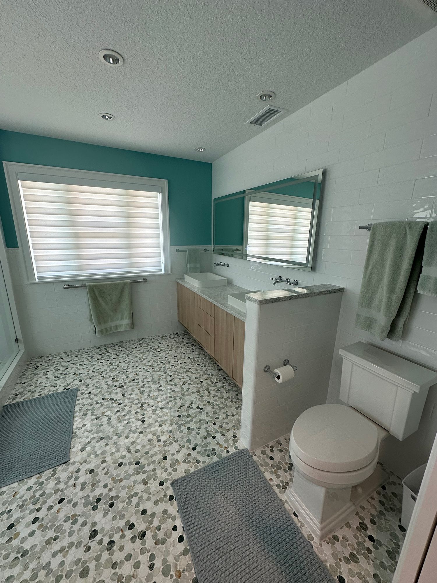 Bathroom with patterned floor, blue accents, light wood vanity, and a window.