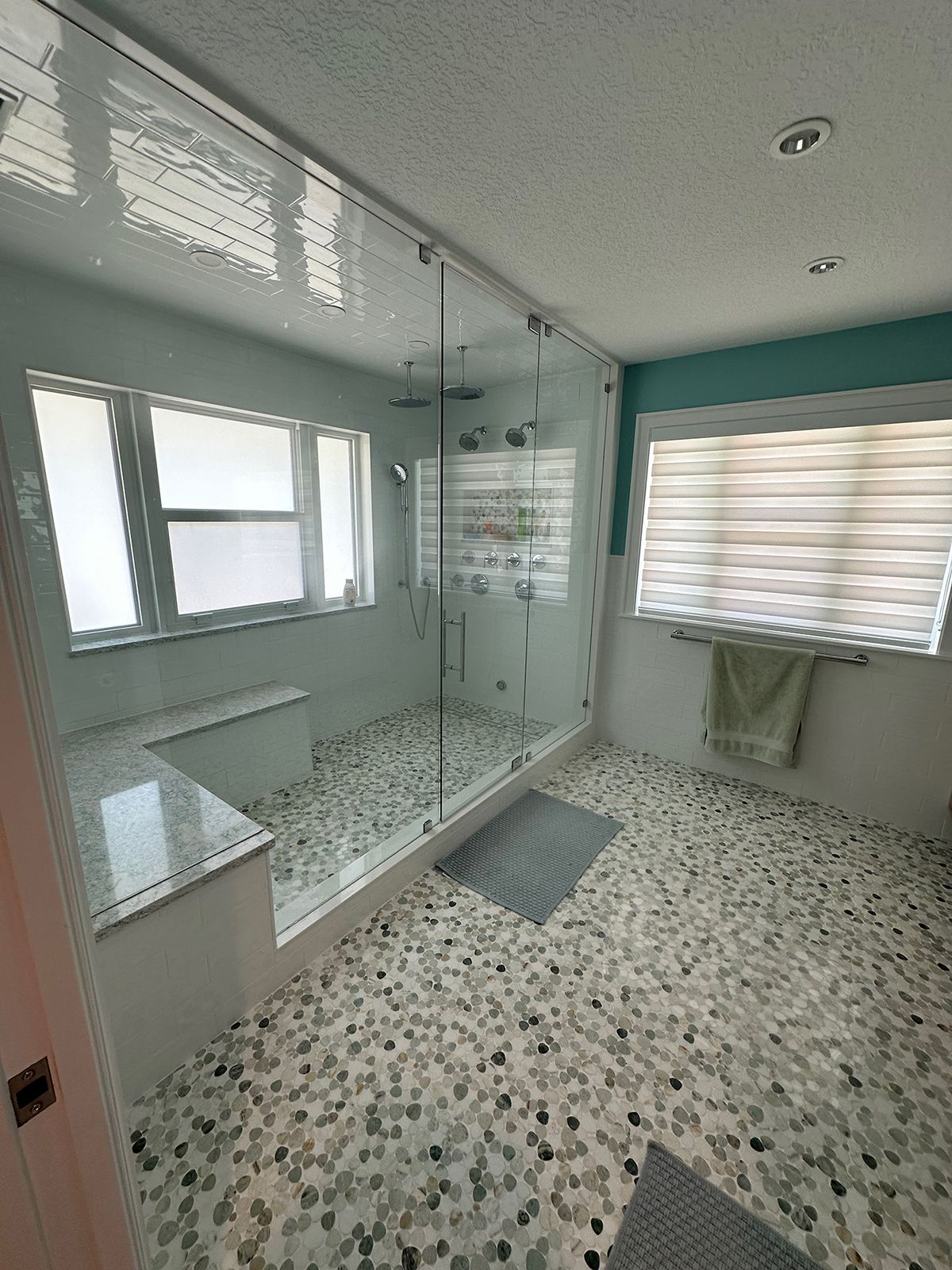 Modern bathroom with glass shower, pebble tile floor, built-in bench, and blue-green walls.